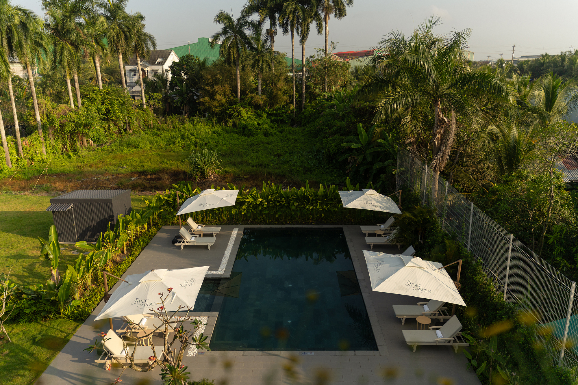 Elevated view of rectangular pool deck with white umbrellas set within lush tropical garden landscape