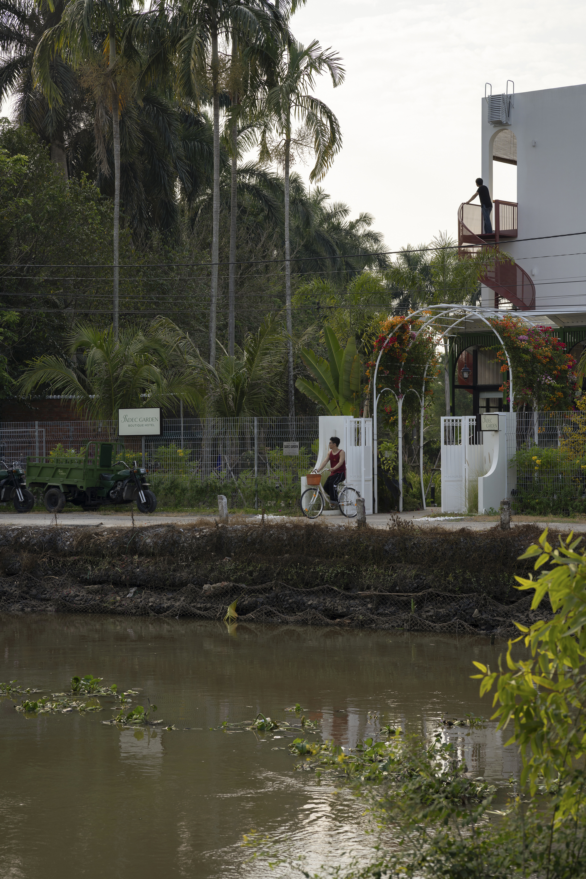 Street view across a canal showing the white arched entry gate with a cyclist passing by
