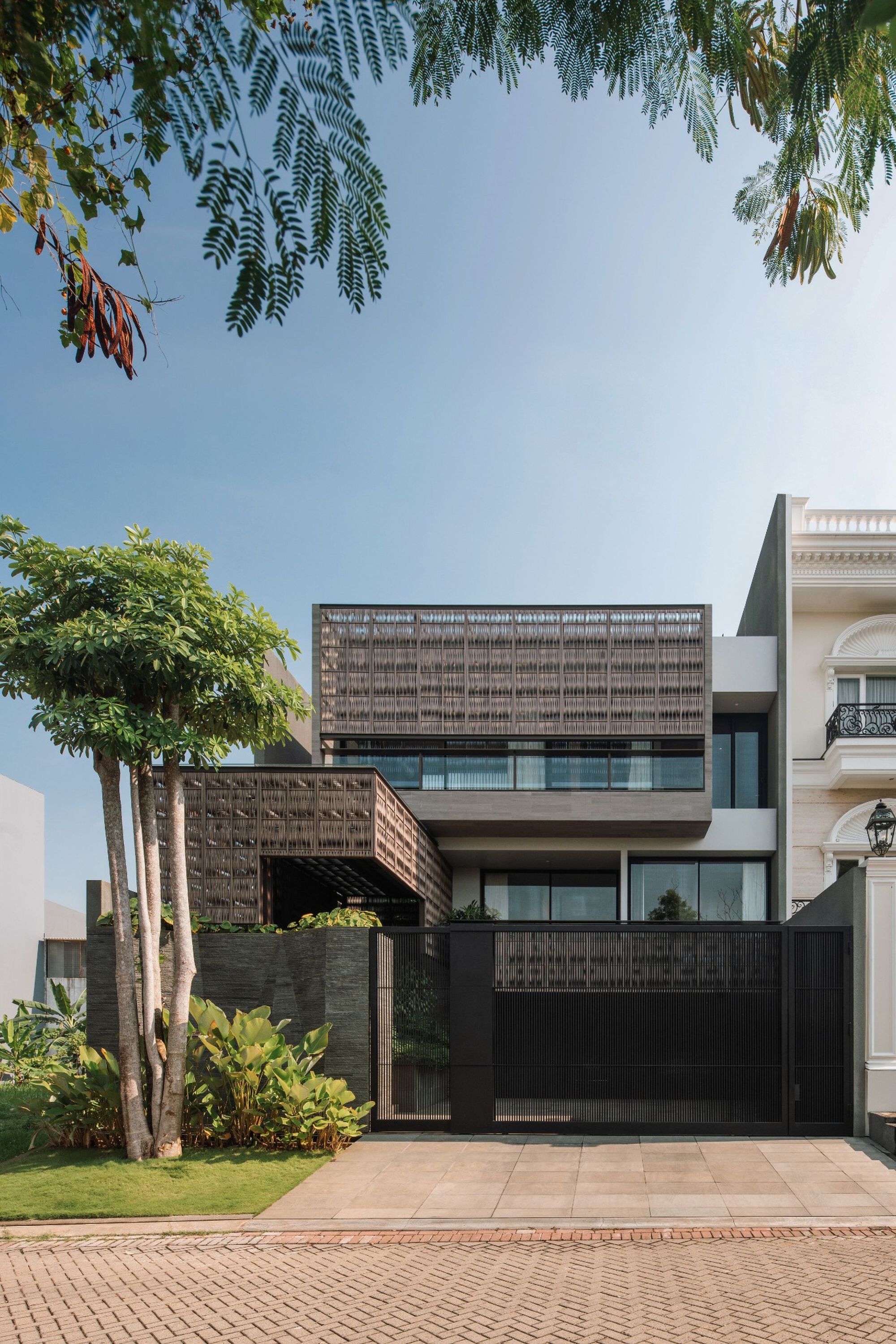 Front elevation showing layered lattice screens and cantilevered upper volume seen through leafy tree branches