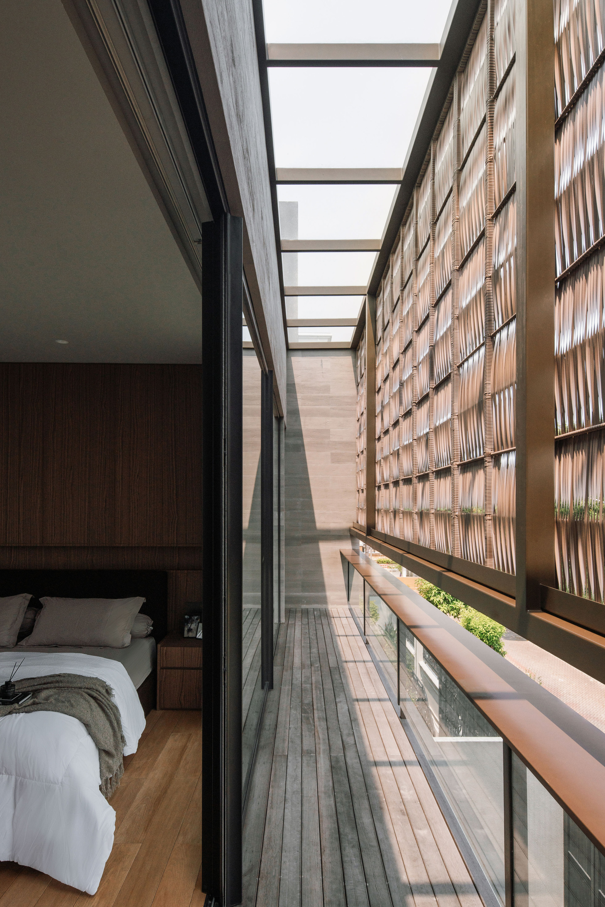 Narrow balcony with timber decking running alongside a bedroom and screened by a woven lattice wall