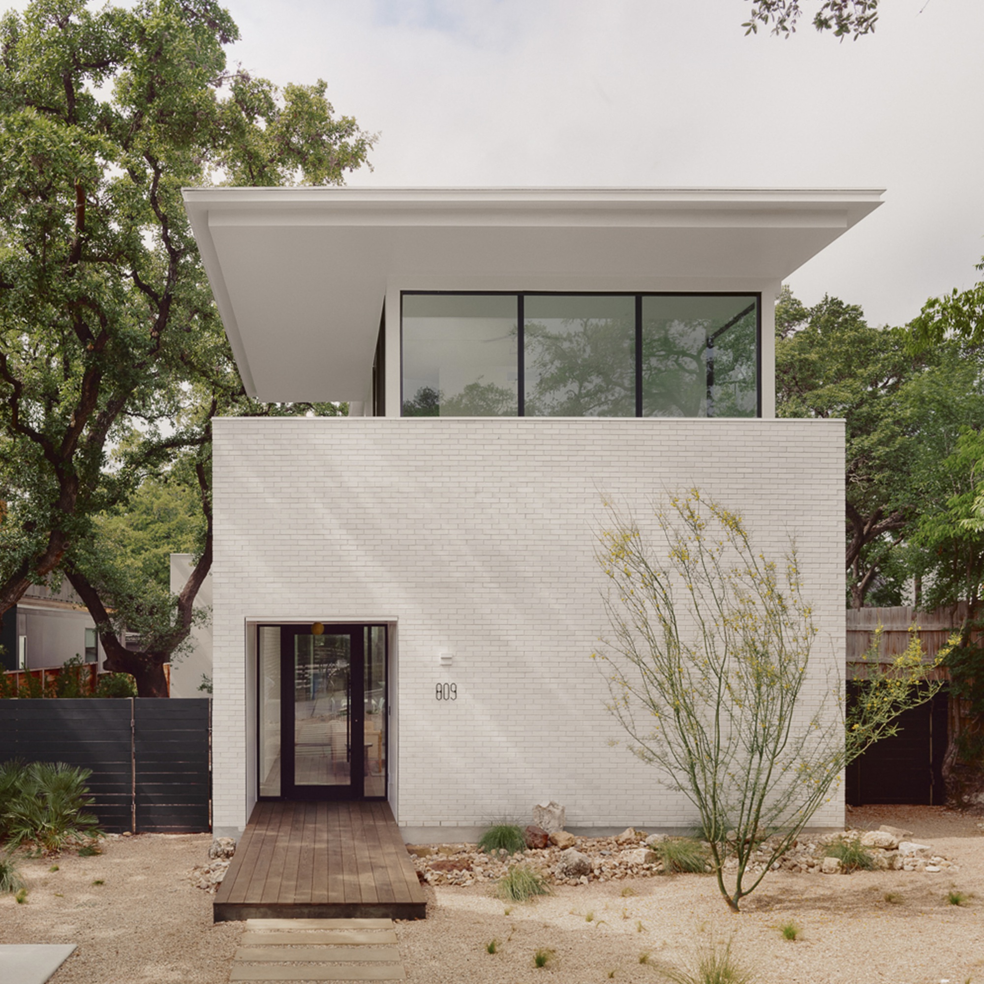 Street facade with white brick and recessed glazed entry flanked by a desert landscape with grasses