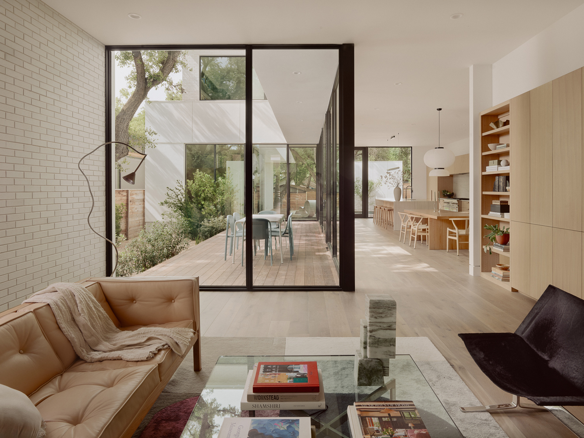 Living area opening to a courtyard through floor-to-ceiling glazed doors with white brick wall