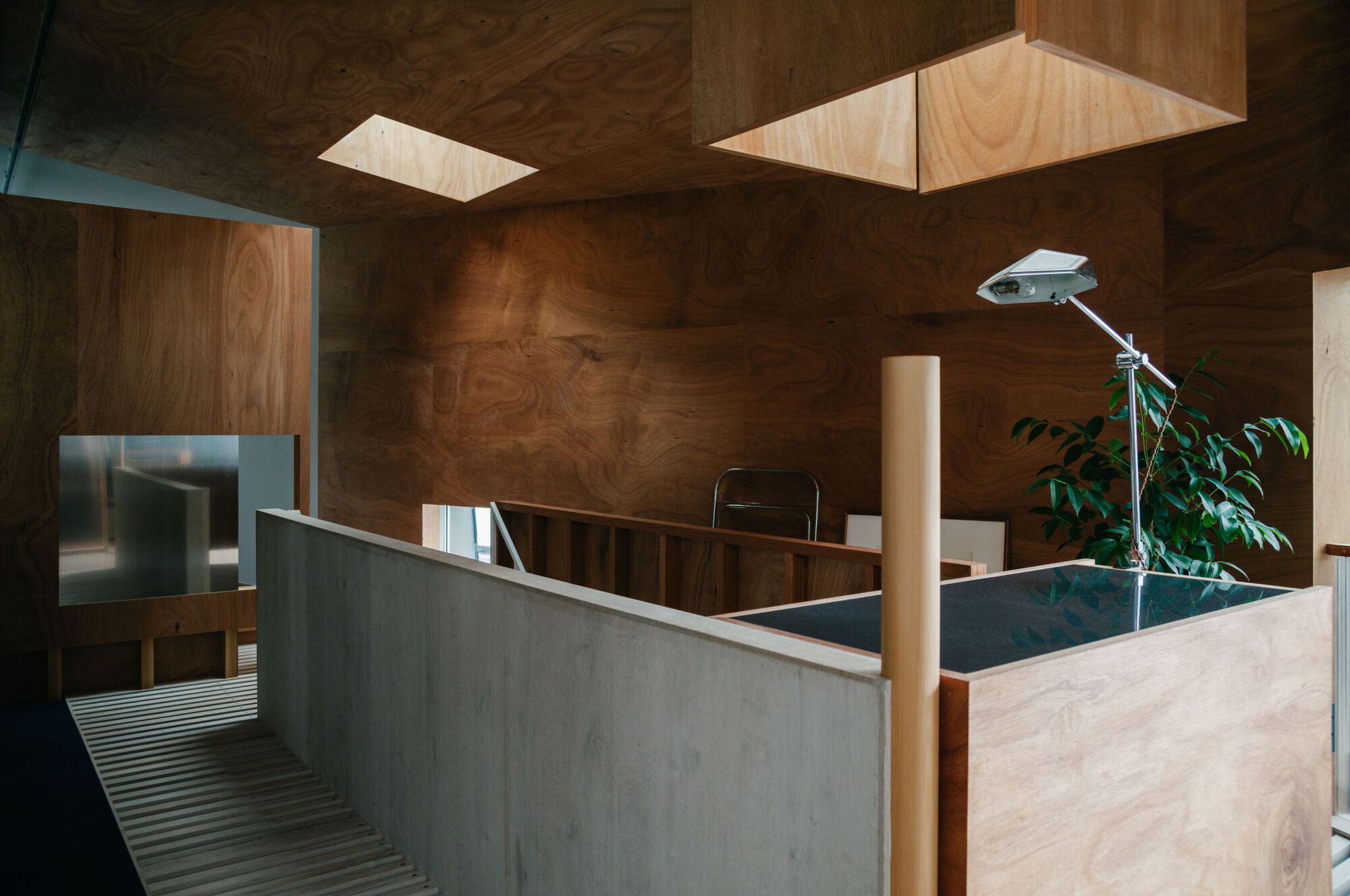 Upper level with plywood walls and ceiling, concrete balustrade, and skylights above a planted interior courtyard