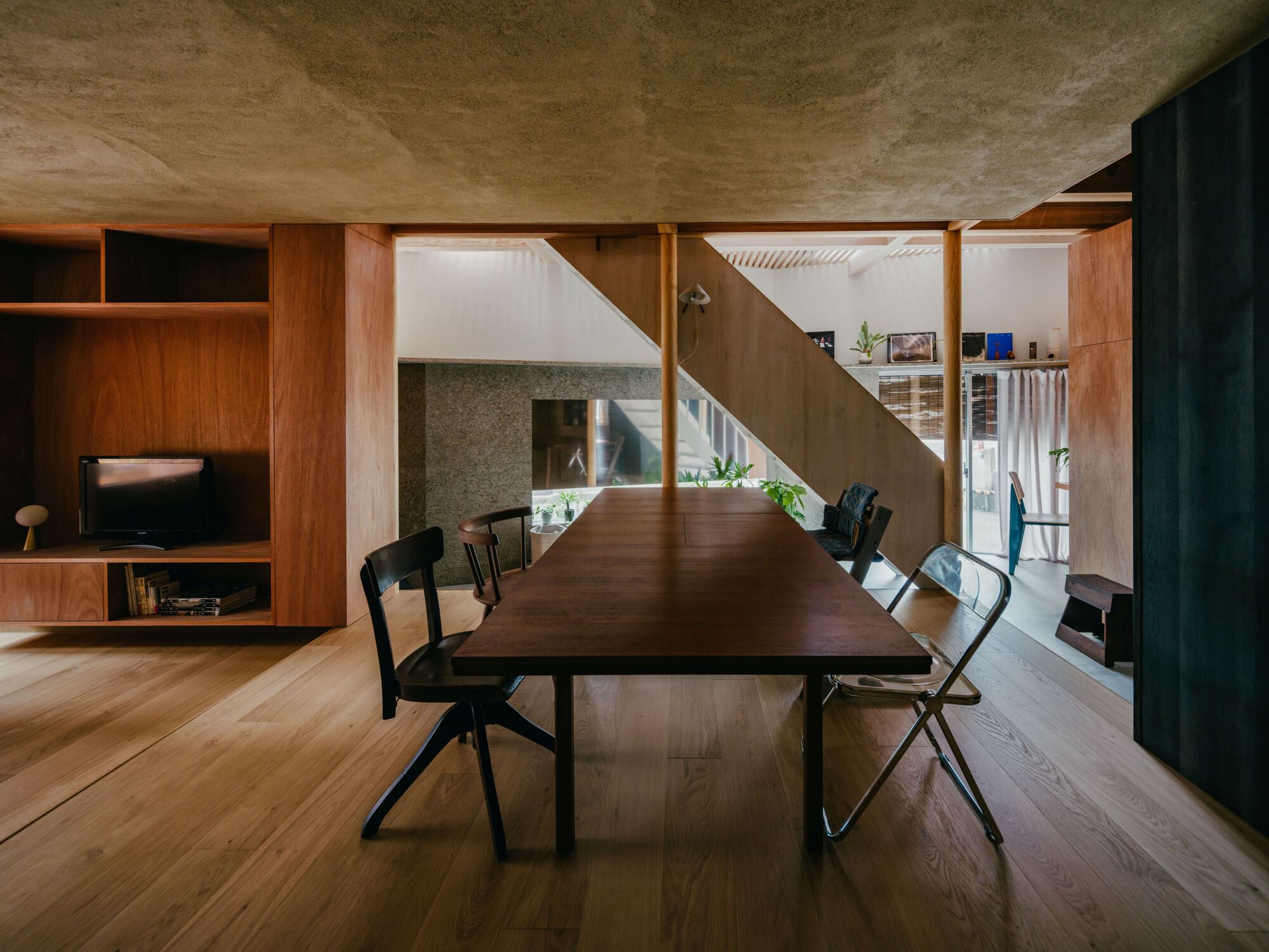 Dining area with timber table beneath exposed plywood ceiling and staircase connecting to open shelving above