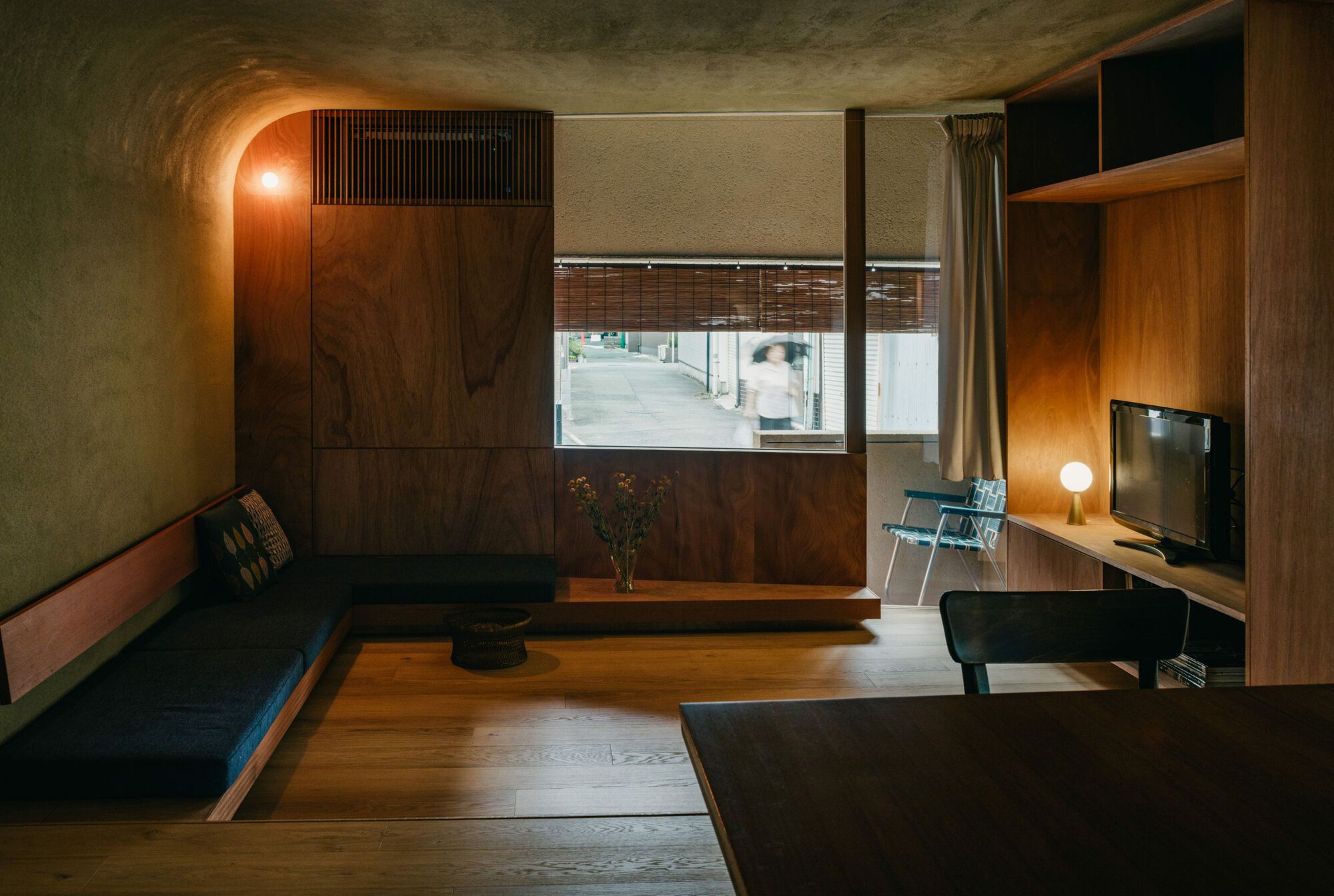 Living room with curved plywood ceiling, timber cabinetry, and a window overlooking the street at dusk