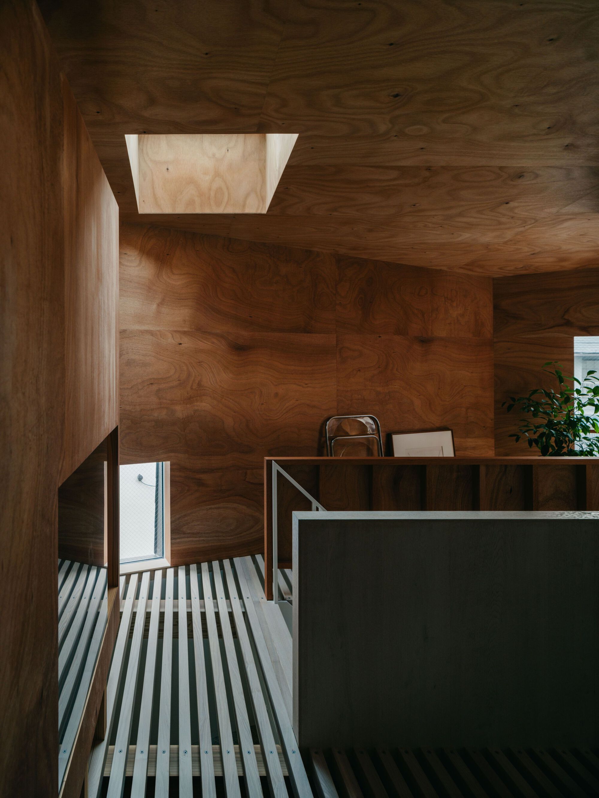 Upper landing with slatted metal flooring and a square skylight above plywood-clad walls