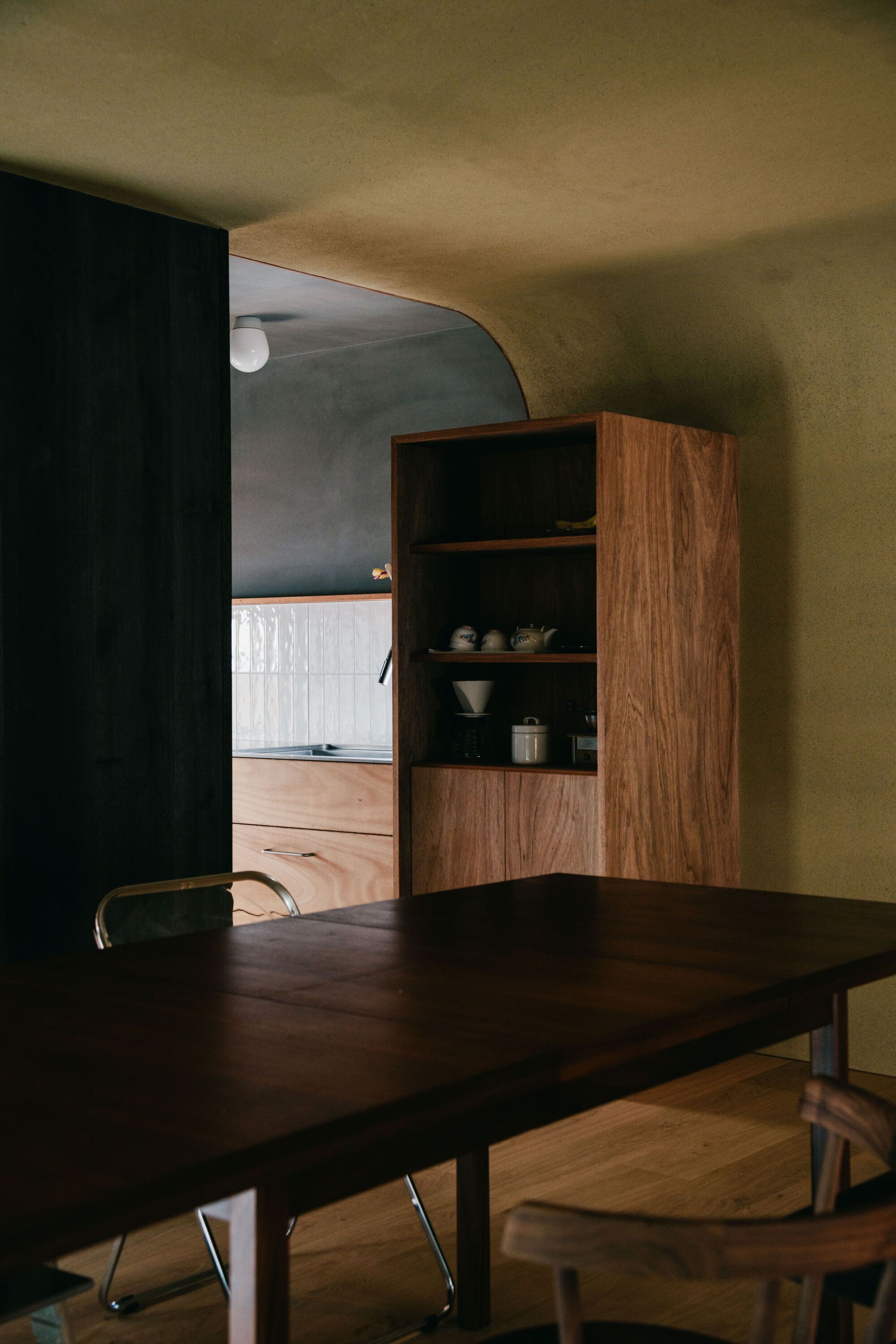 Walnut dining table and built-in shelving with arched doorway opening to adjacent room