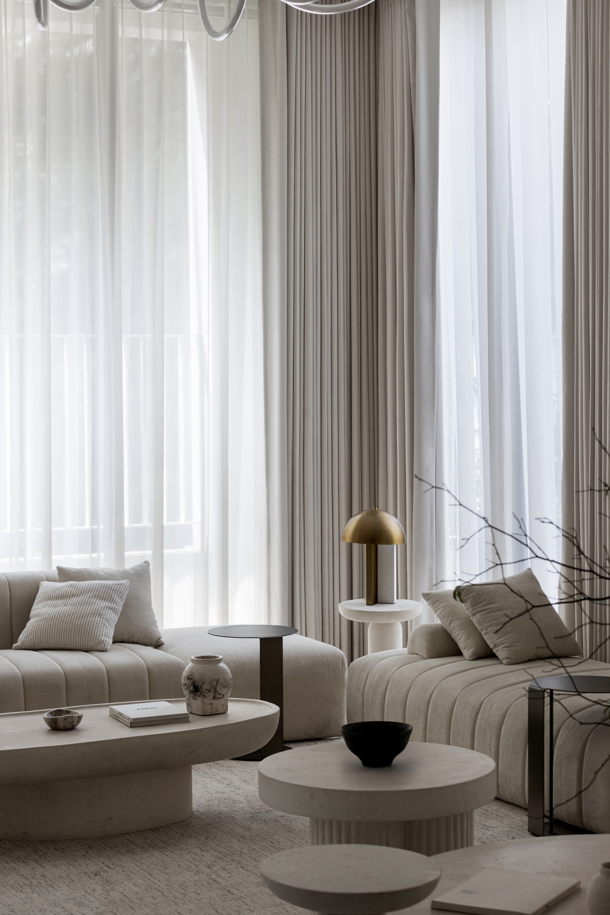 Living area with layered sheer curtains filtering daylight over modular seating and fluted stone tables