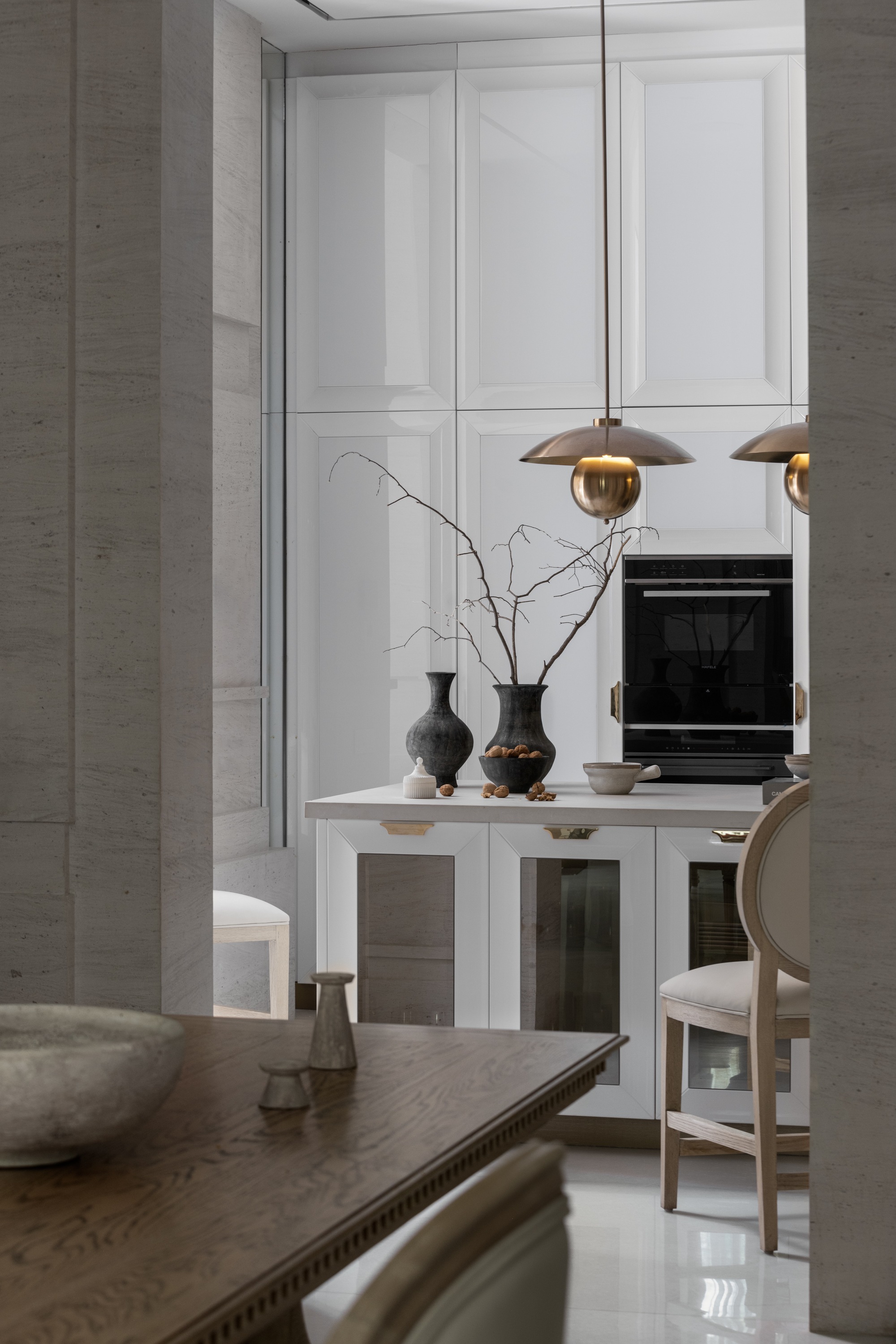Kitchen island with brass pendant lights and decorative branches against white paneled cabinetry