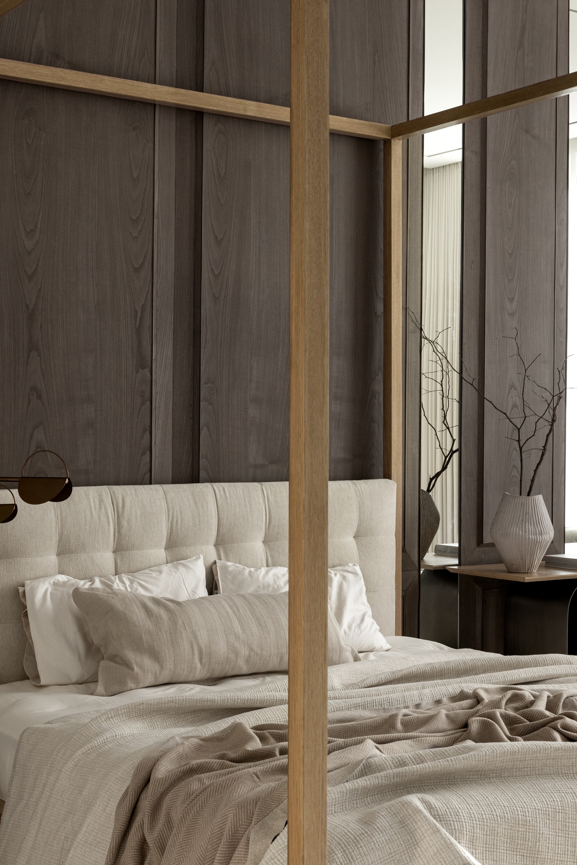 Bedroom with timber-framed canopy bed against dark wood paneled walls and sheer curtains