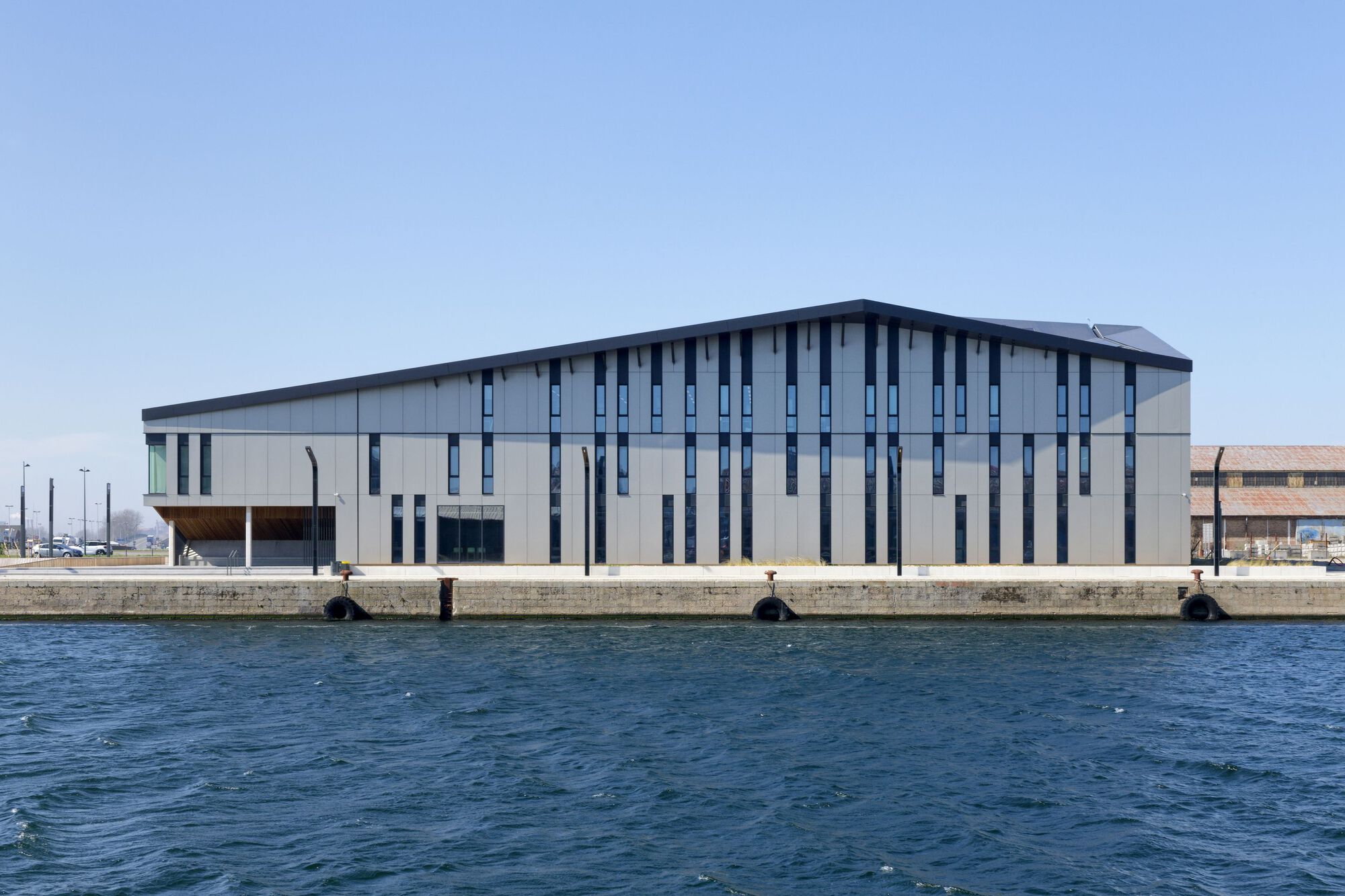 Waterside elevation with vertical window slots and metal cladding seen from across the harbor