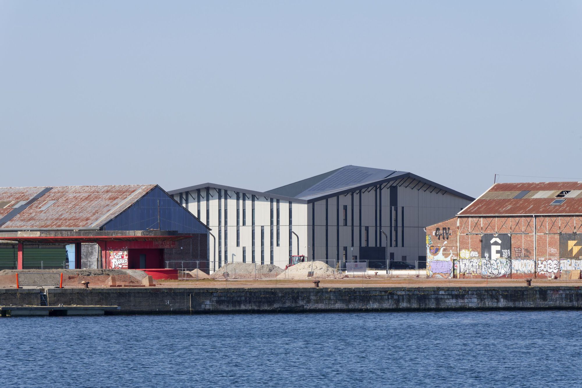 Cluster of pitched-roof volumes with varied cladding beside weathered brick warehouses along the quay