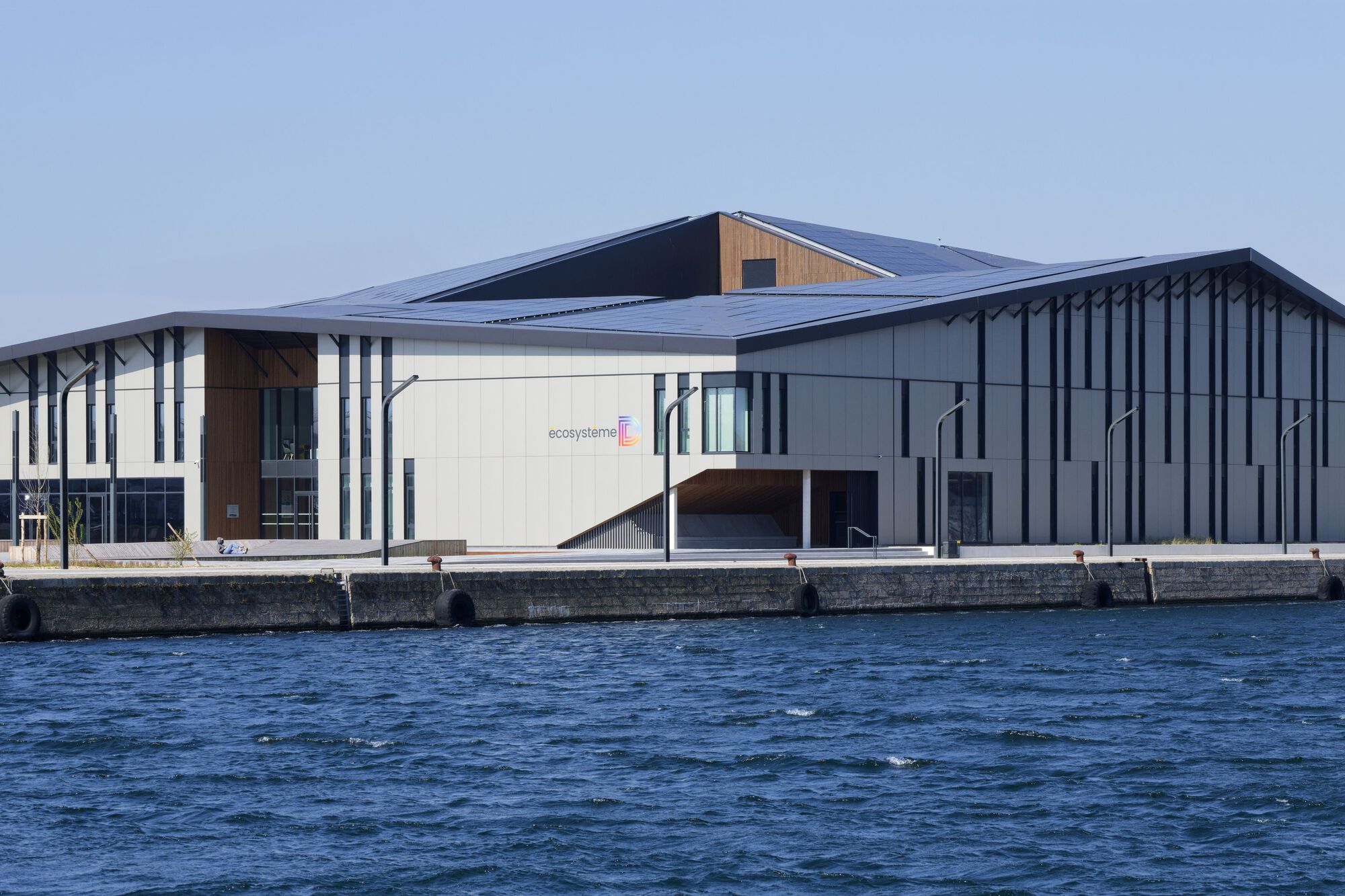 Waterfront facade with vertical metal fins and clerestory timber volume under a clear sky