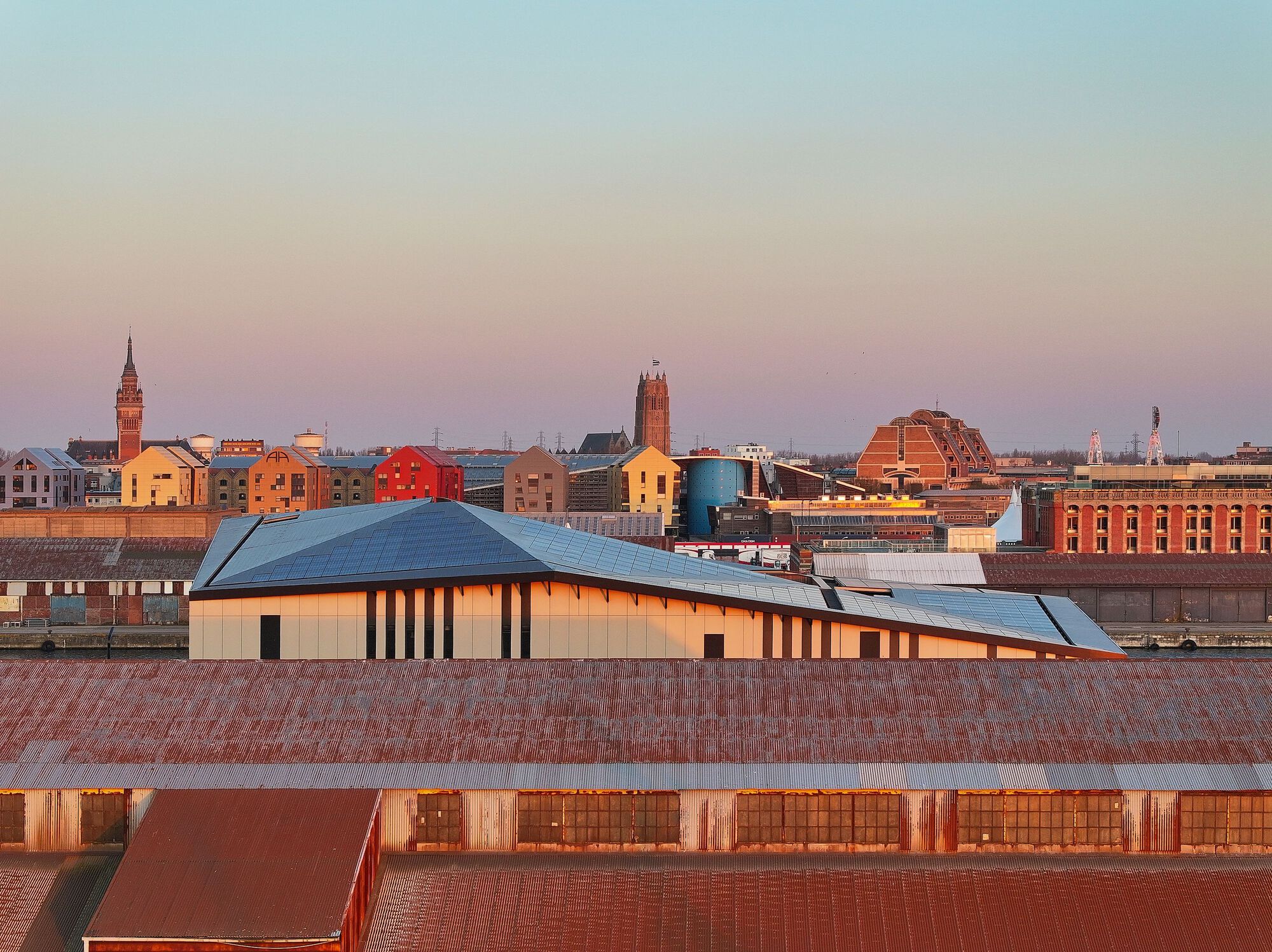 Roofscape perspective with the solar panel roof volume emerging above brick warehouse rooftops at twilight