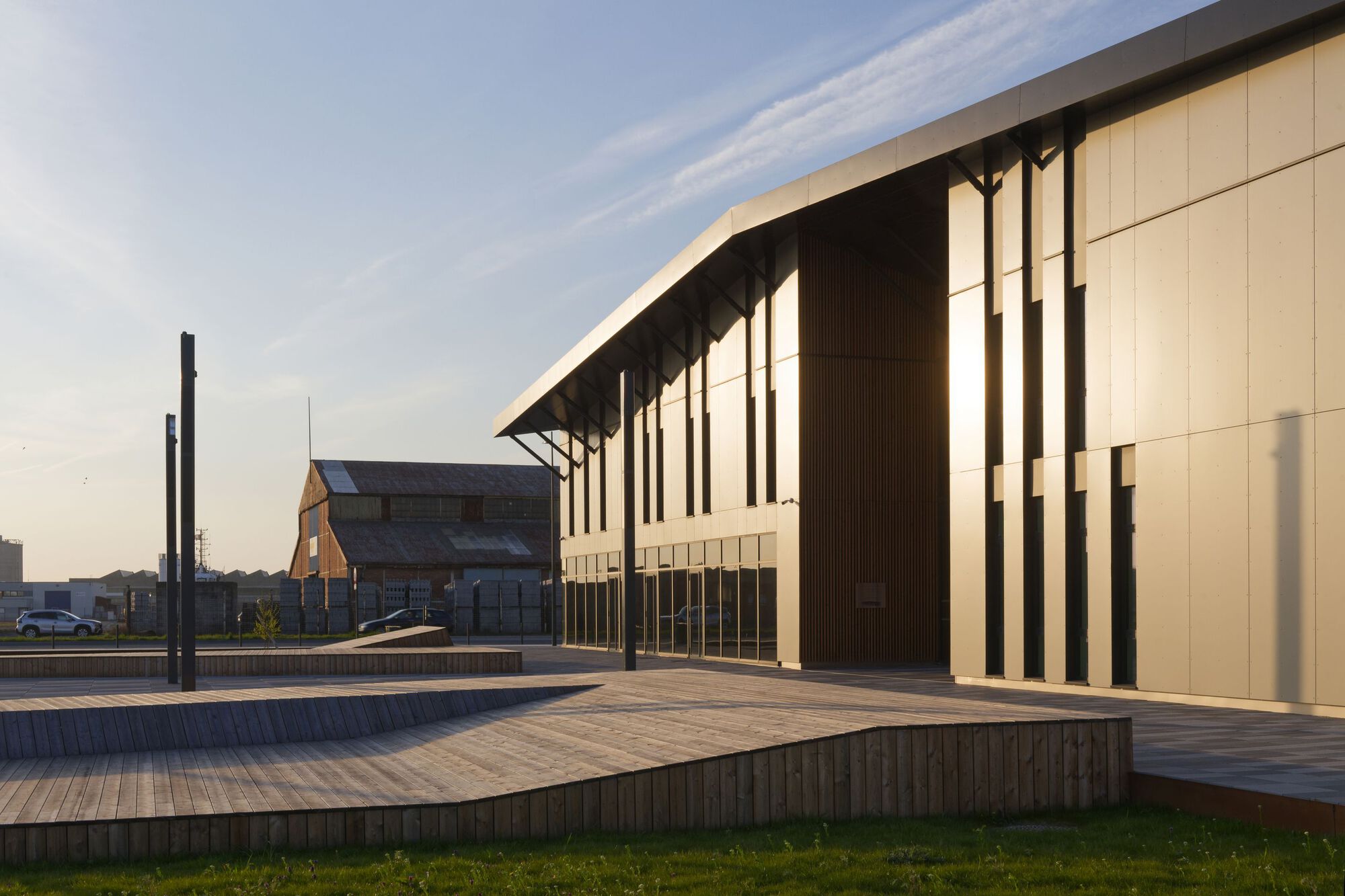 Timber-decked plaza in front of the slatted facade with deep overhang at golden hour