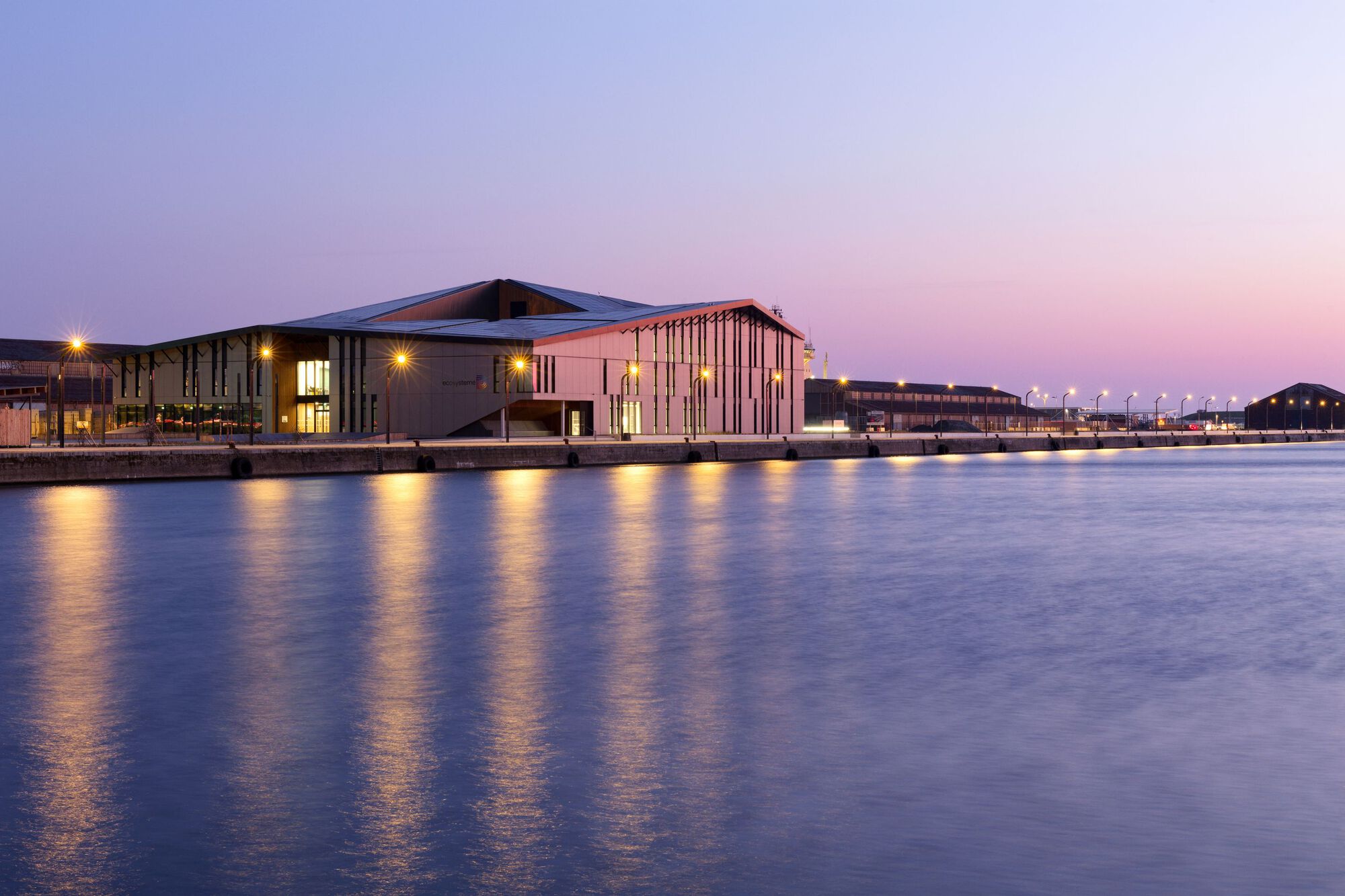Long waterfront elevation with illuminated windows and slat detailing under a violet twilight sky
