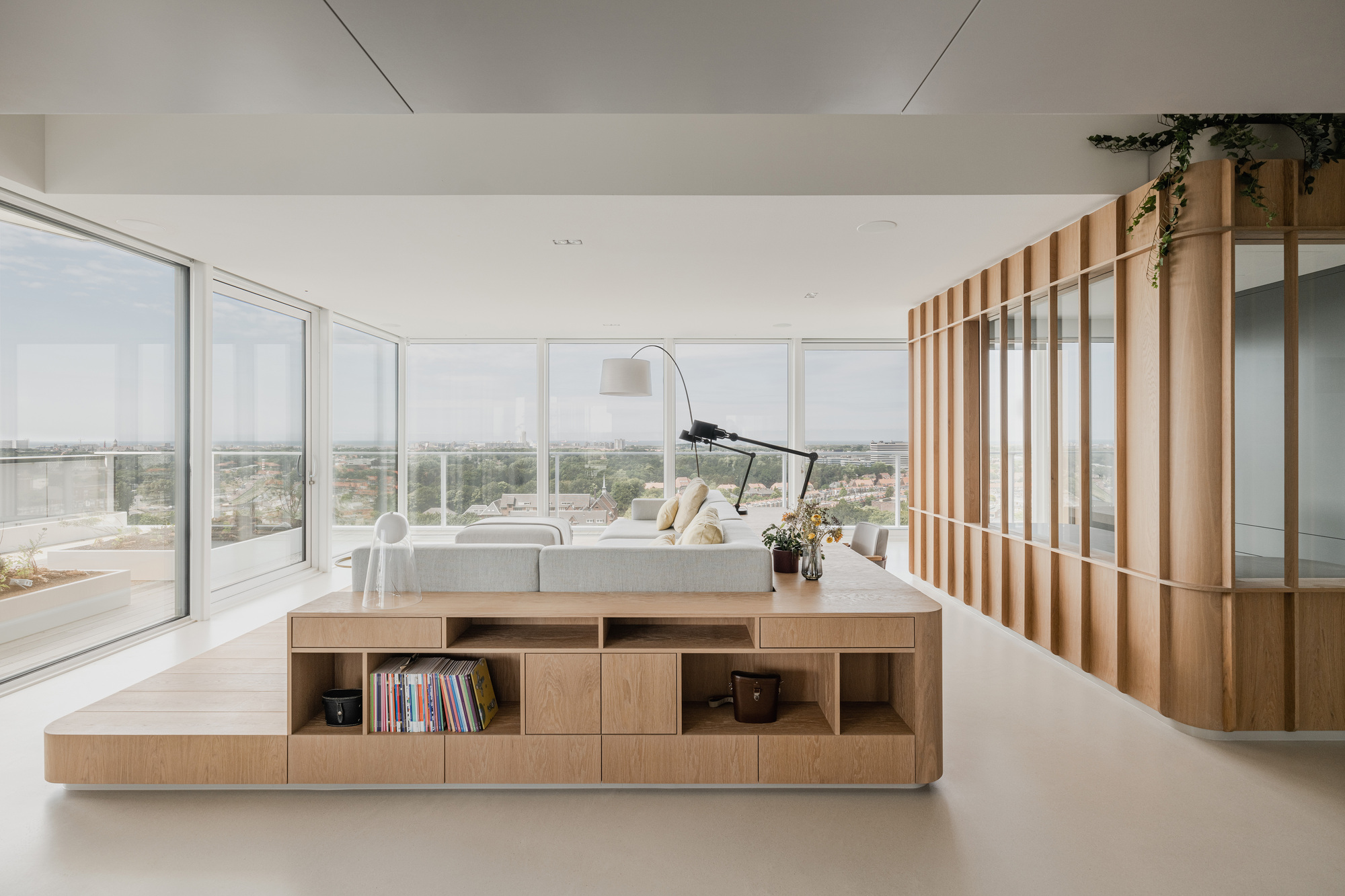 Elevated timber platform with integrated seating and storage facing floor-to-ceiling windows overlooking distant greenery