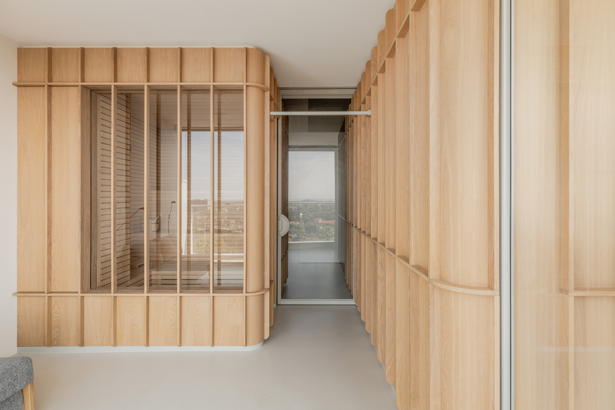 Corridor flanked by curved timber paneling with glass inserts revealing a distant cityscape