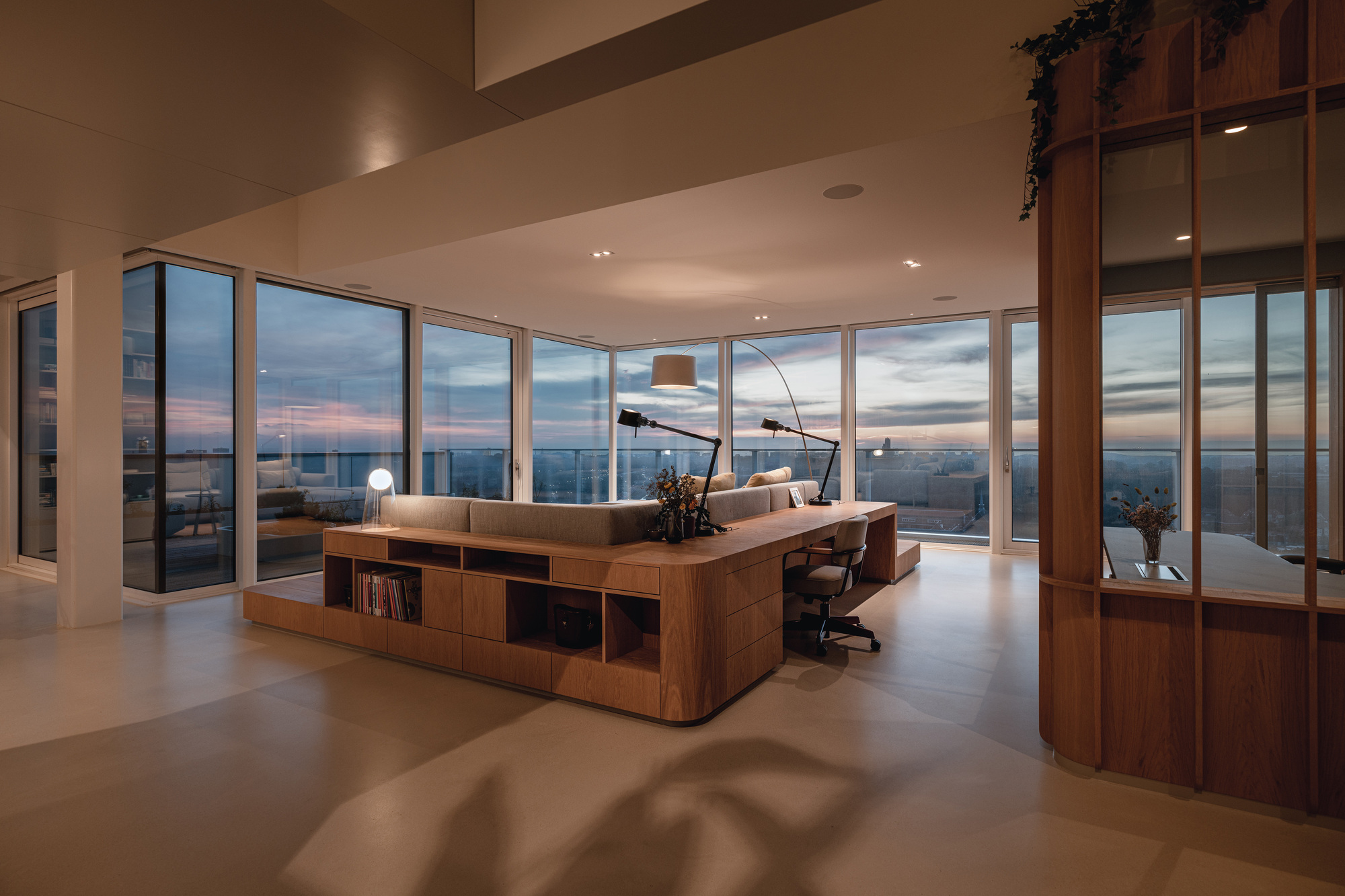 Open living space with floor-to-ceiling glazing overlooking the city at dusk