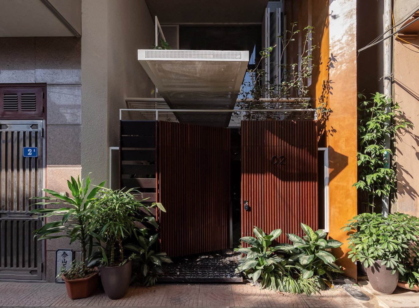 Narrow entrance courtyard with corrugated metal gate panels and potted plants under stacked concrete balconies