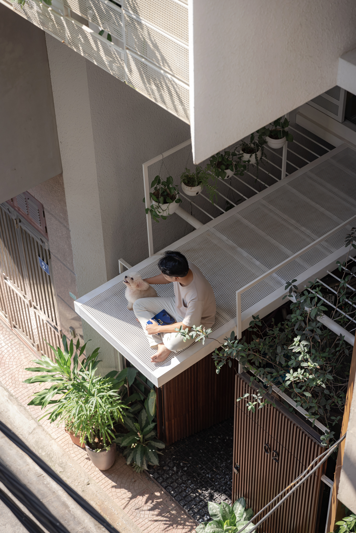 Overhead view of resident seated on perforated metal balcony platform surrounded by planters and pebble ground