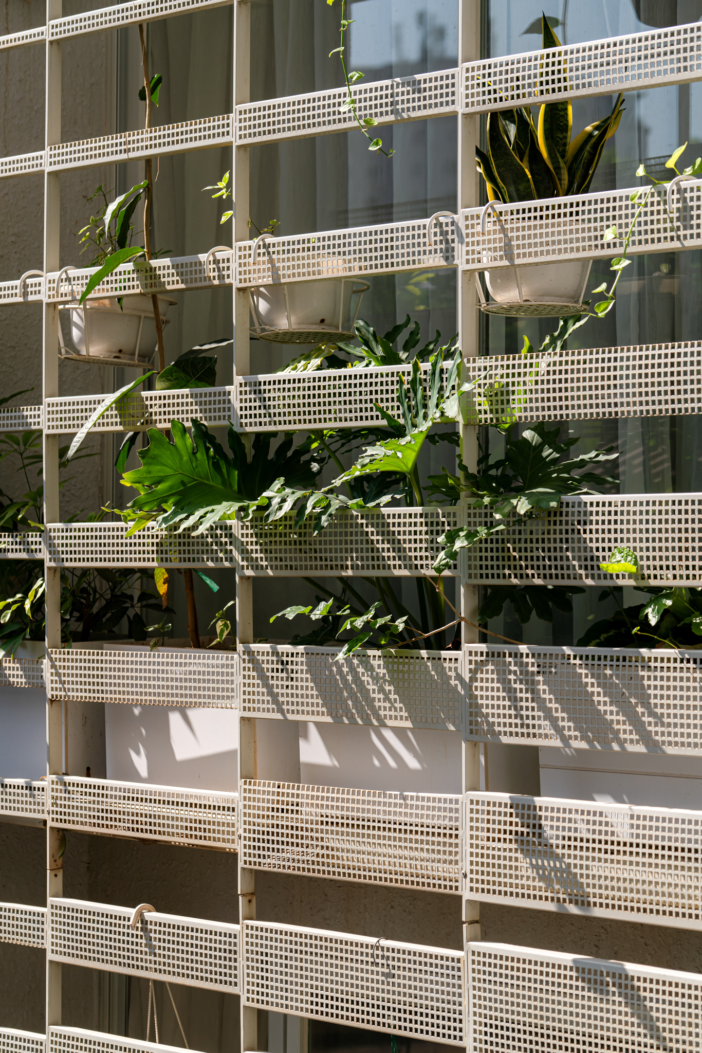 Facade detail of stacked white perforated metal screens with tropical plants growing between the horizontal bands