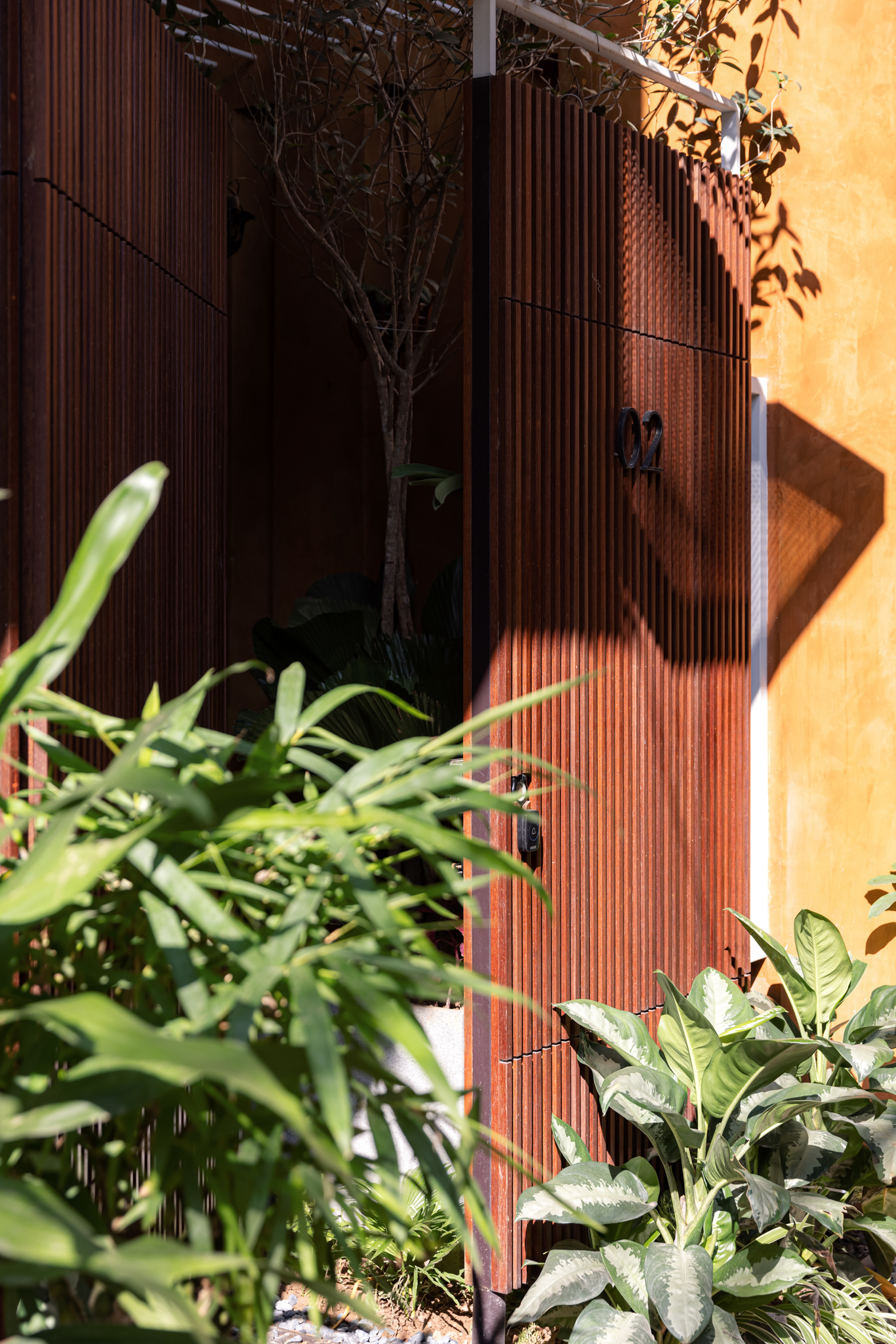 Close-up of the vertical timber slat door with shadows and surrounding tropical foliage