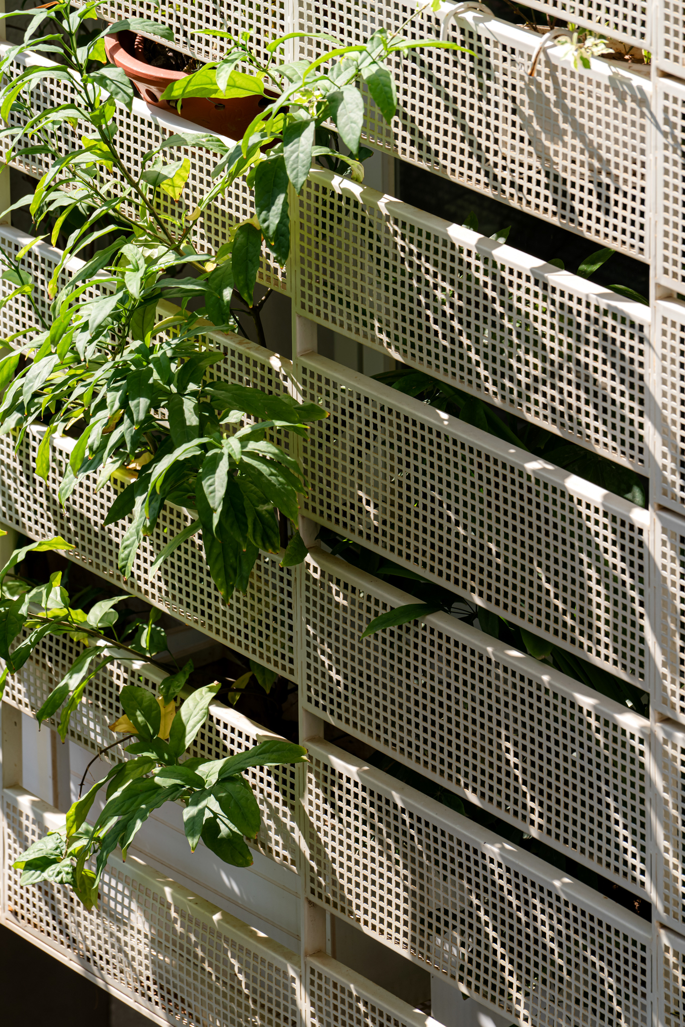 Perforated white metal screen panels with planted balconies visible through the openings