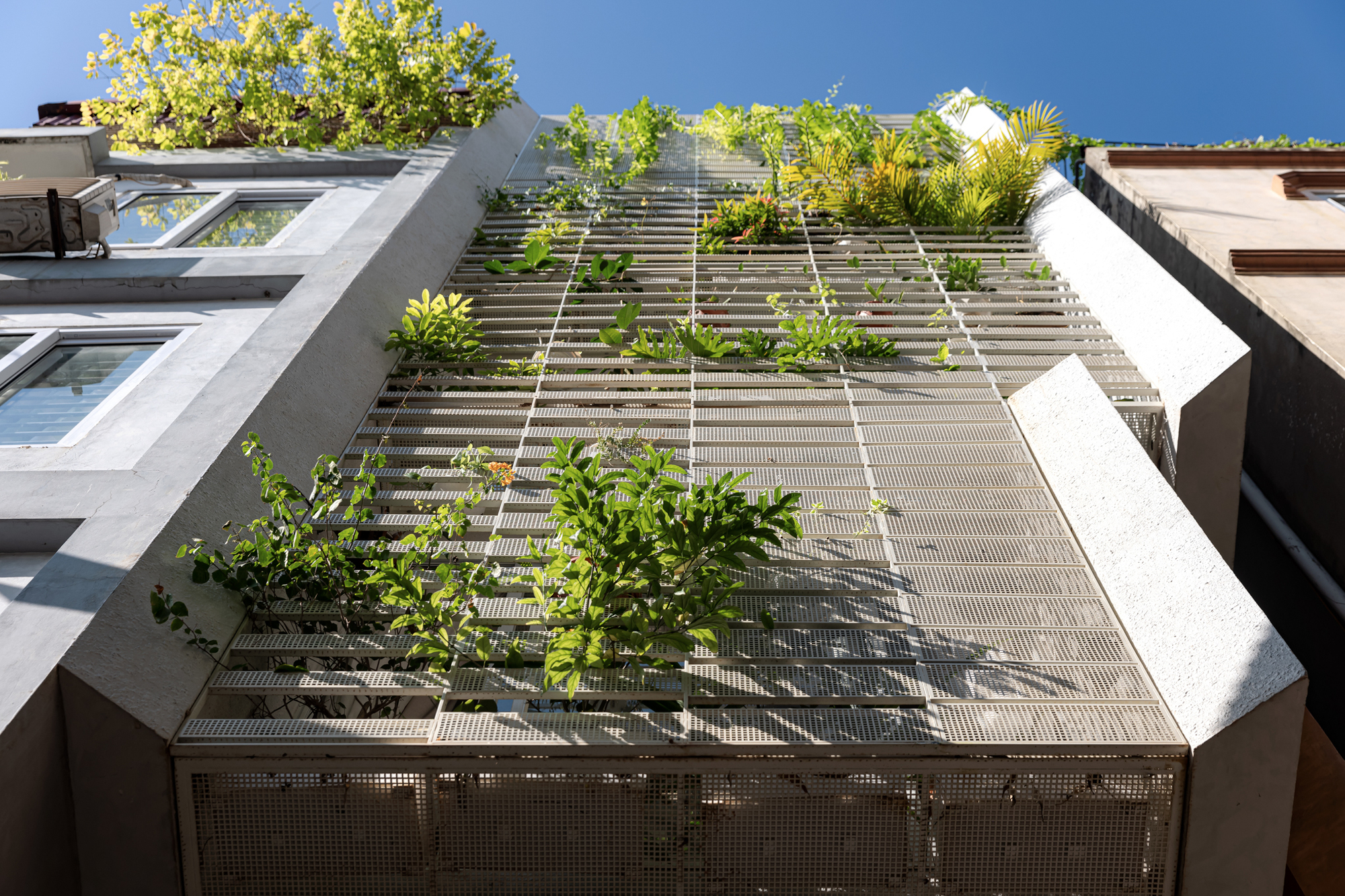 Upward view of the perforated metal facade with planted terraces against a clear blue sky