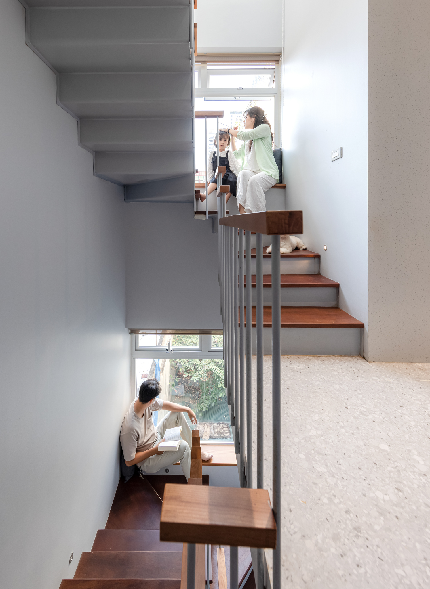 Split-level staircase with timber treads, steel-and-wood balustrade, and figures seated at window landings