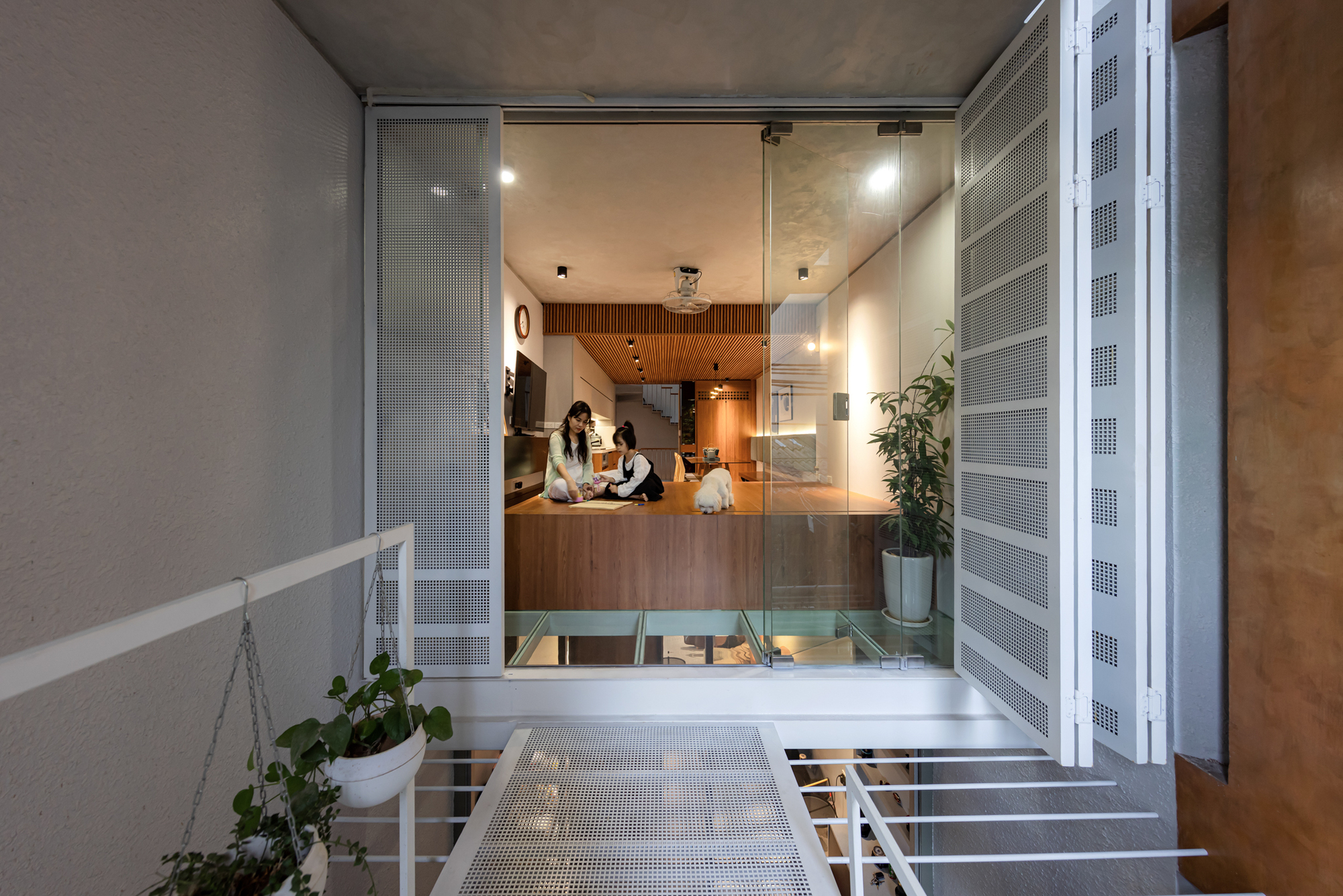Aerial walkway with perforated metal grating bridging across an interior void to the kitchen beyond