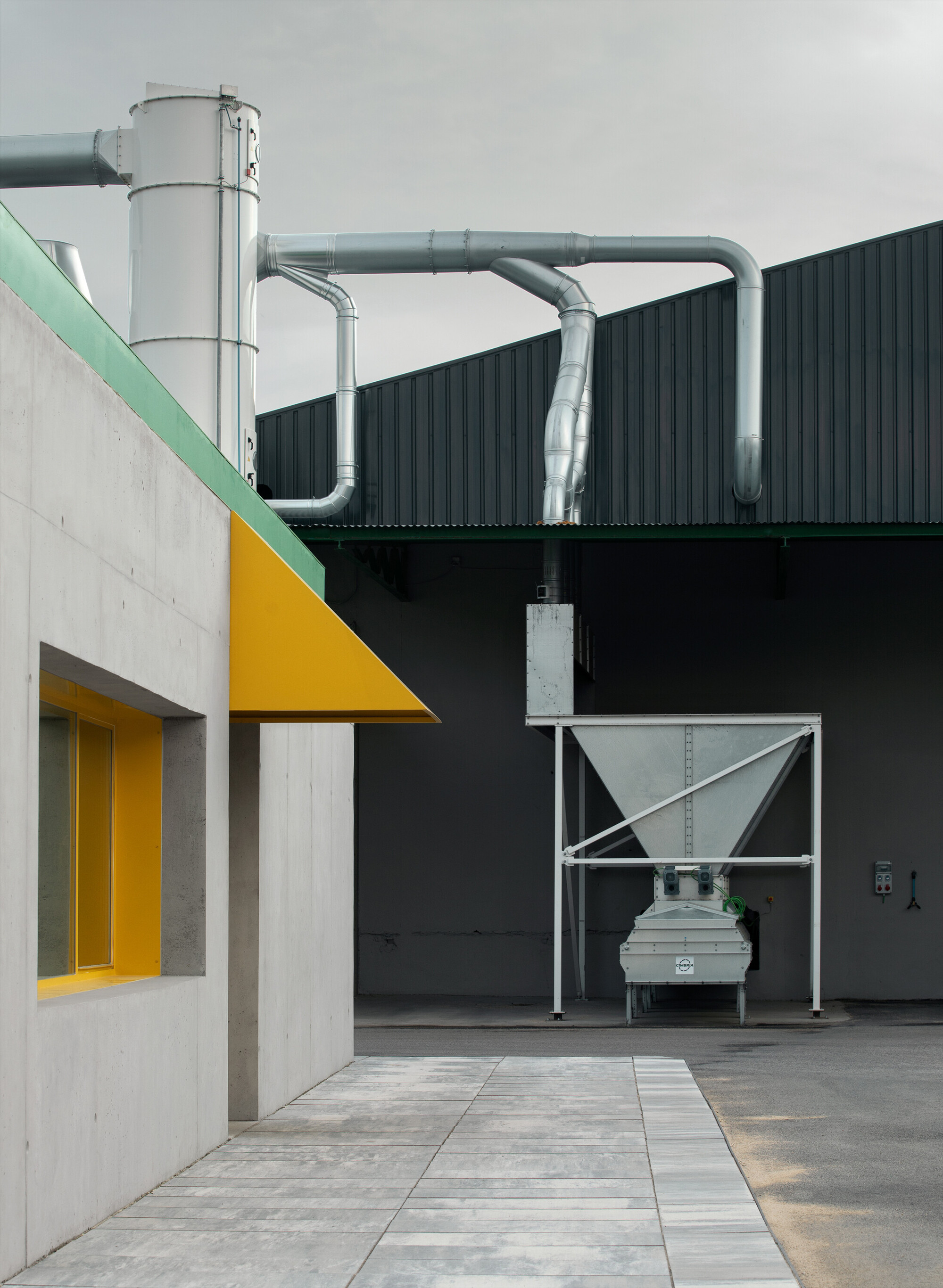 Yellow triangular canopy over concrete entrance with metal ducts and hopper equipment visible behind