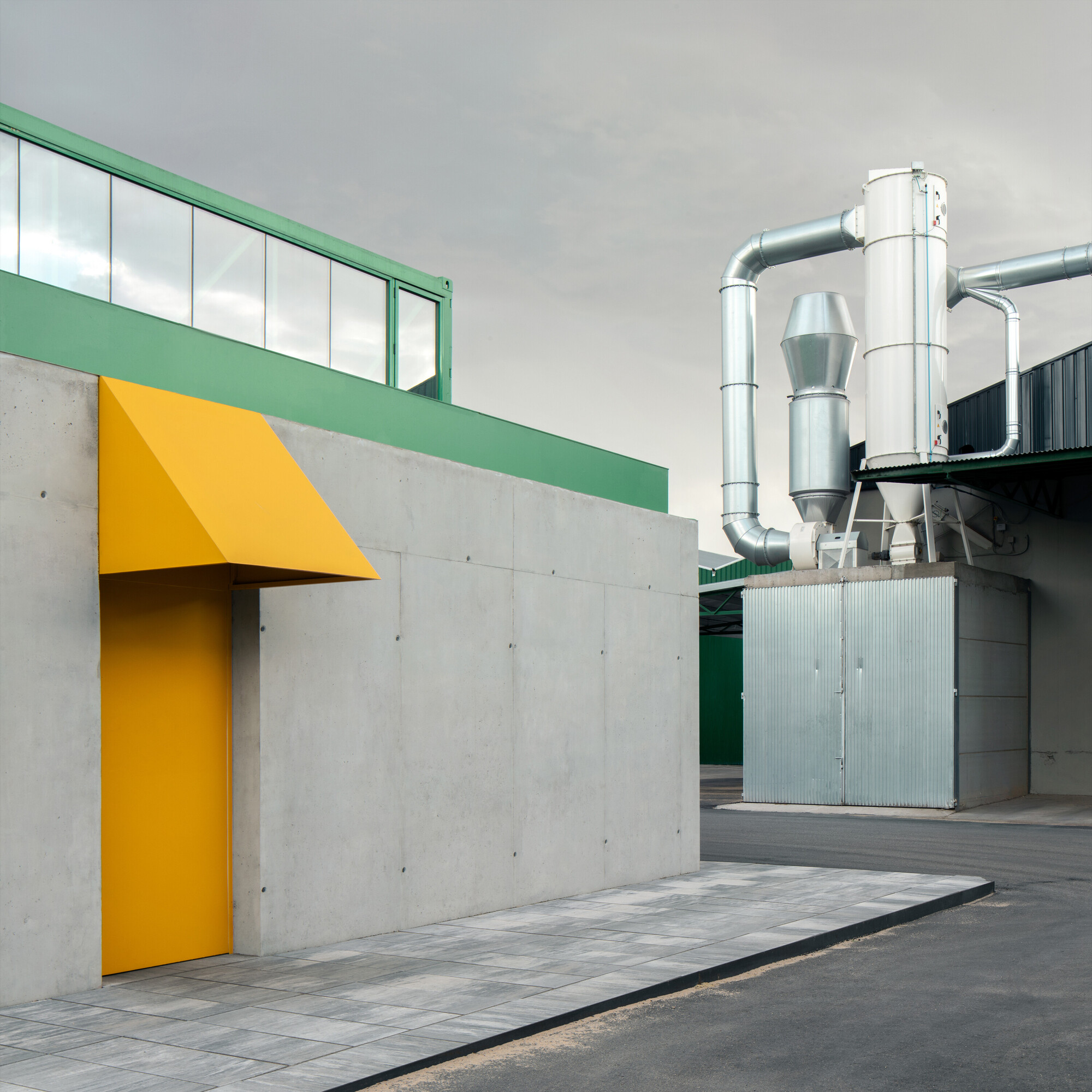 Yellow canopy over entrance in concrete wall with green accents and industrial ductwork beyond