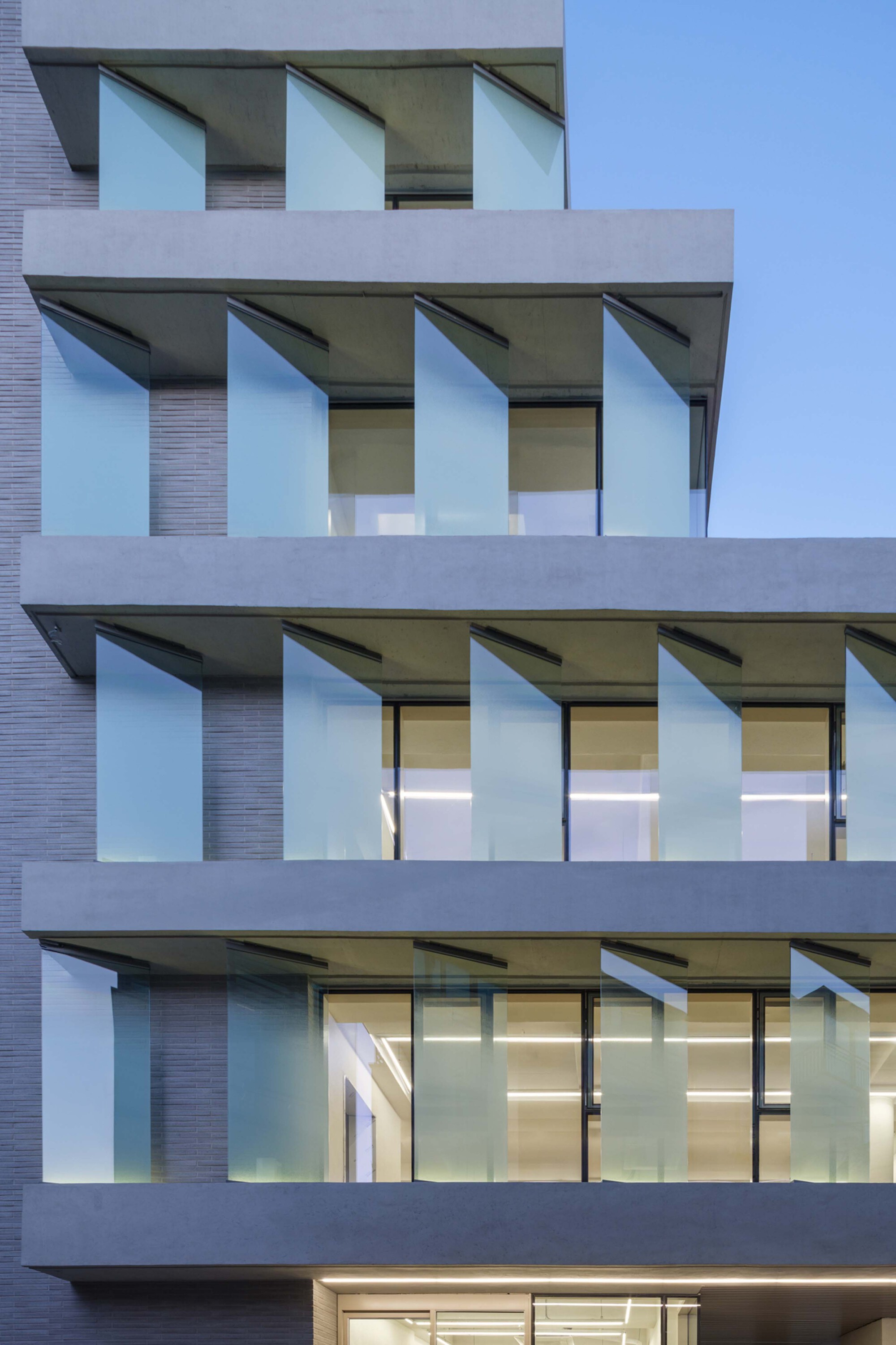 Close-up of the facade balconies with angled glass panels and interior lights visible at dusk