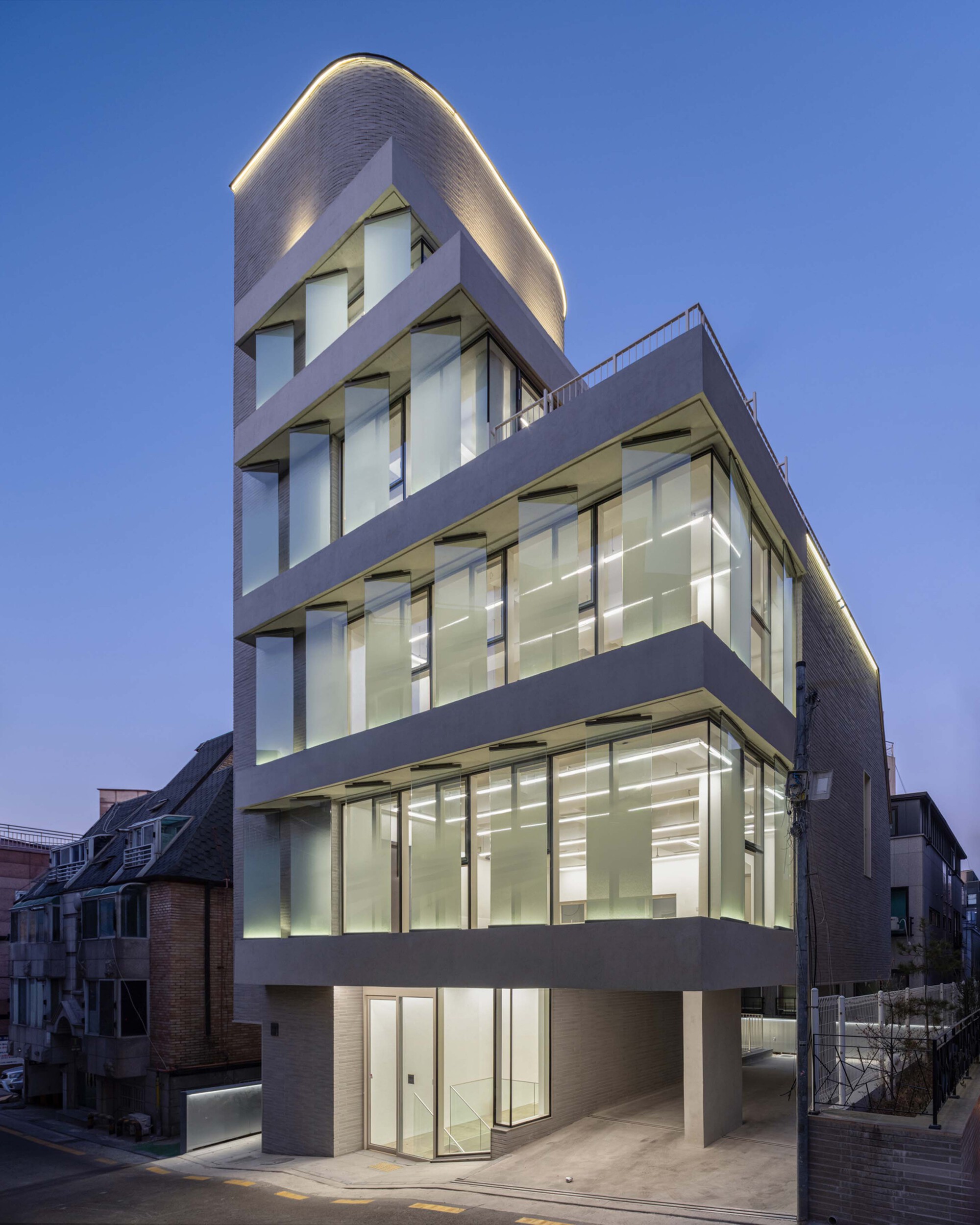 Corner view of the illuminated building at twilight showing the curved brick volume with integrated lighting strips