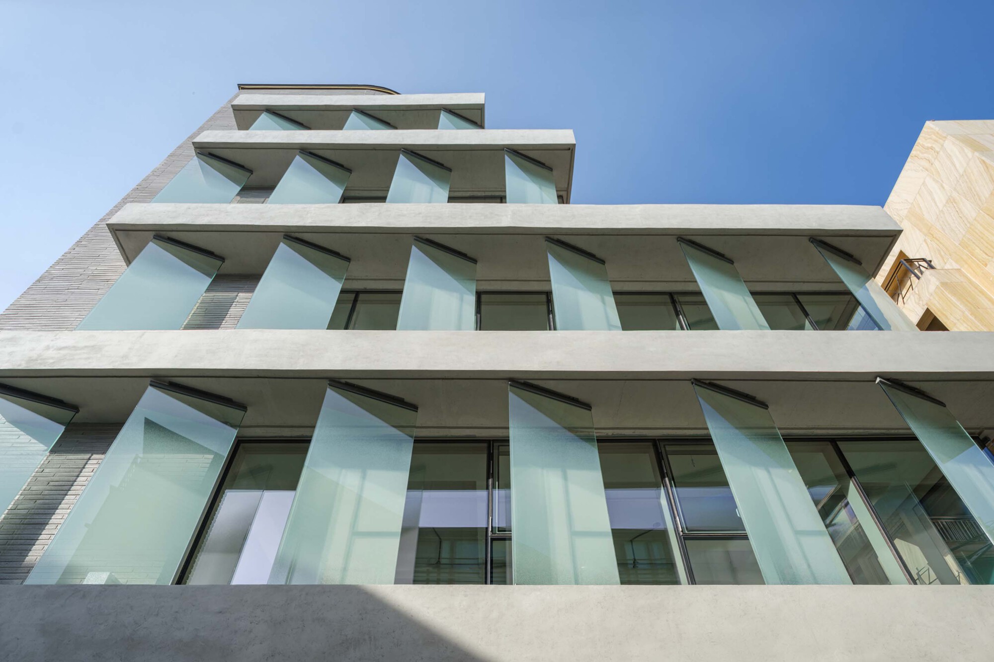 Upward view of the angled glass balconies projecting from white concrete slabs in bright daylight