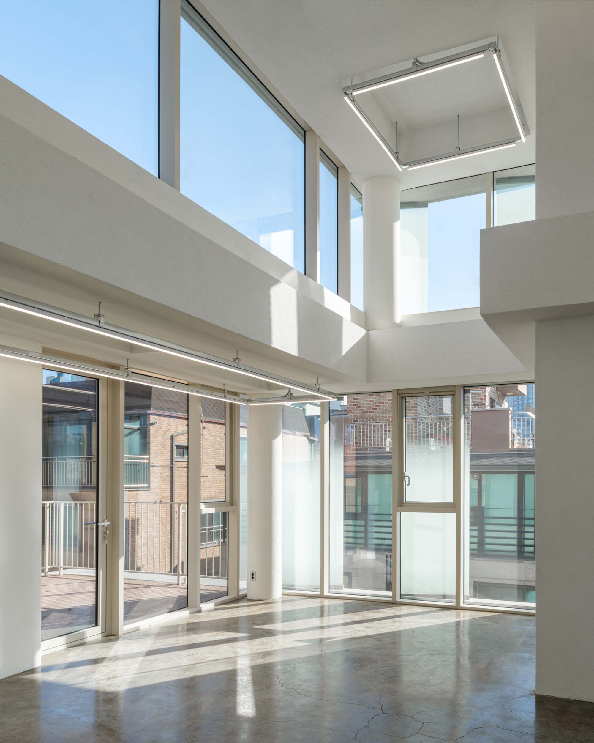 Double height interior space with floor-to-ceiling glass walls and polished concrete flooring catching sunlight