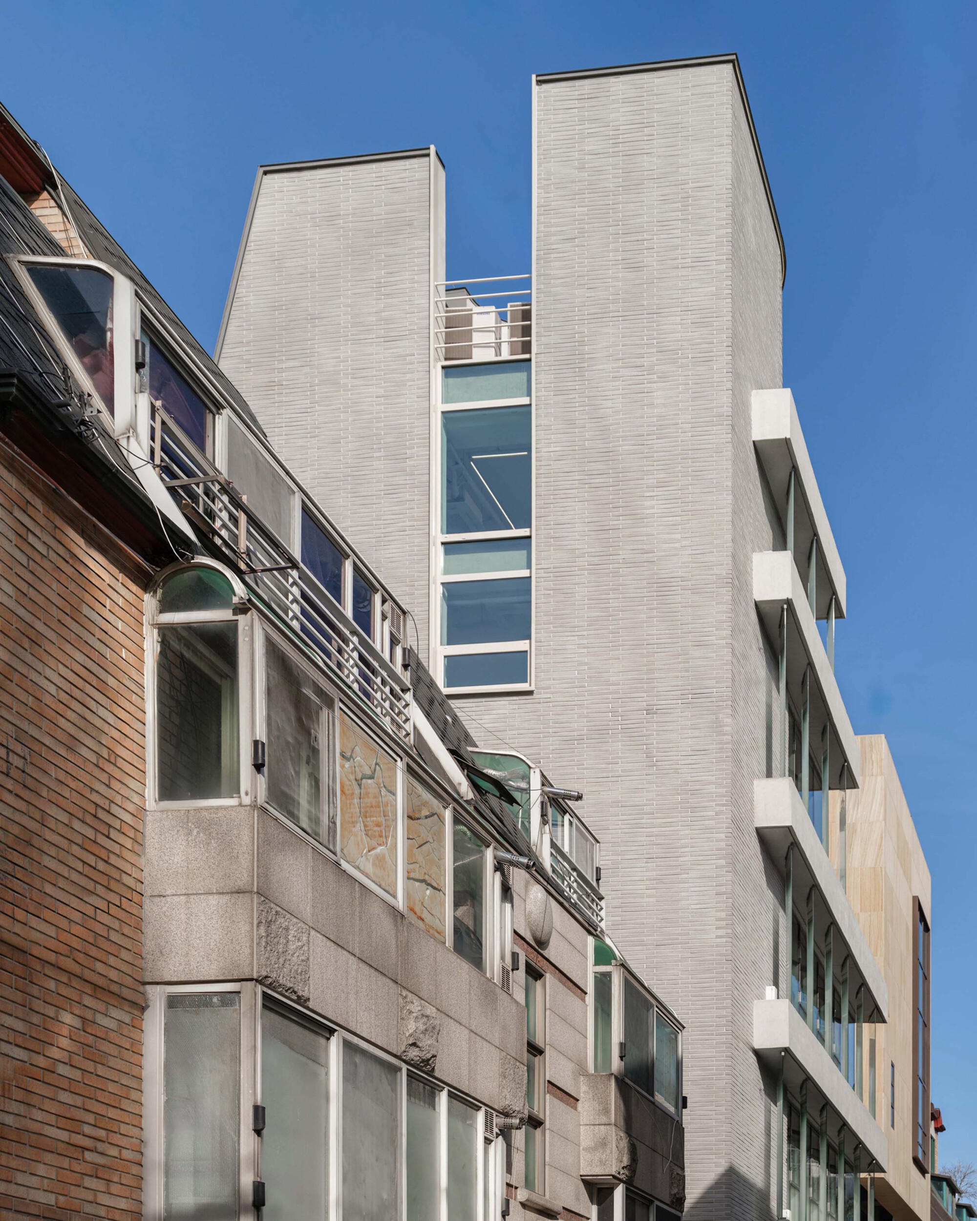 Rear elevation with light grey brick towers flanking a glazed stairwell against neighboring rooftops