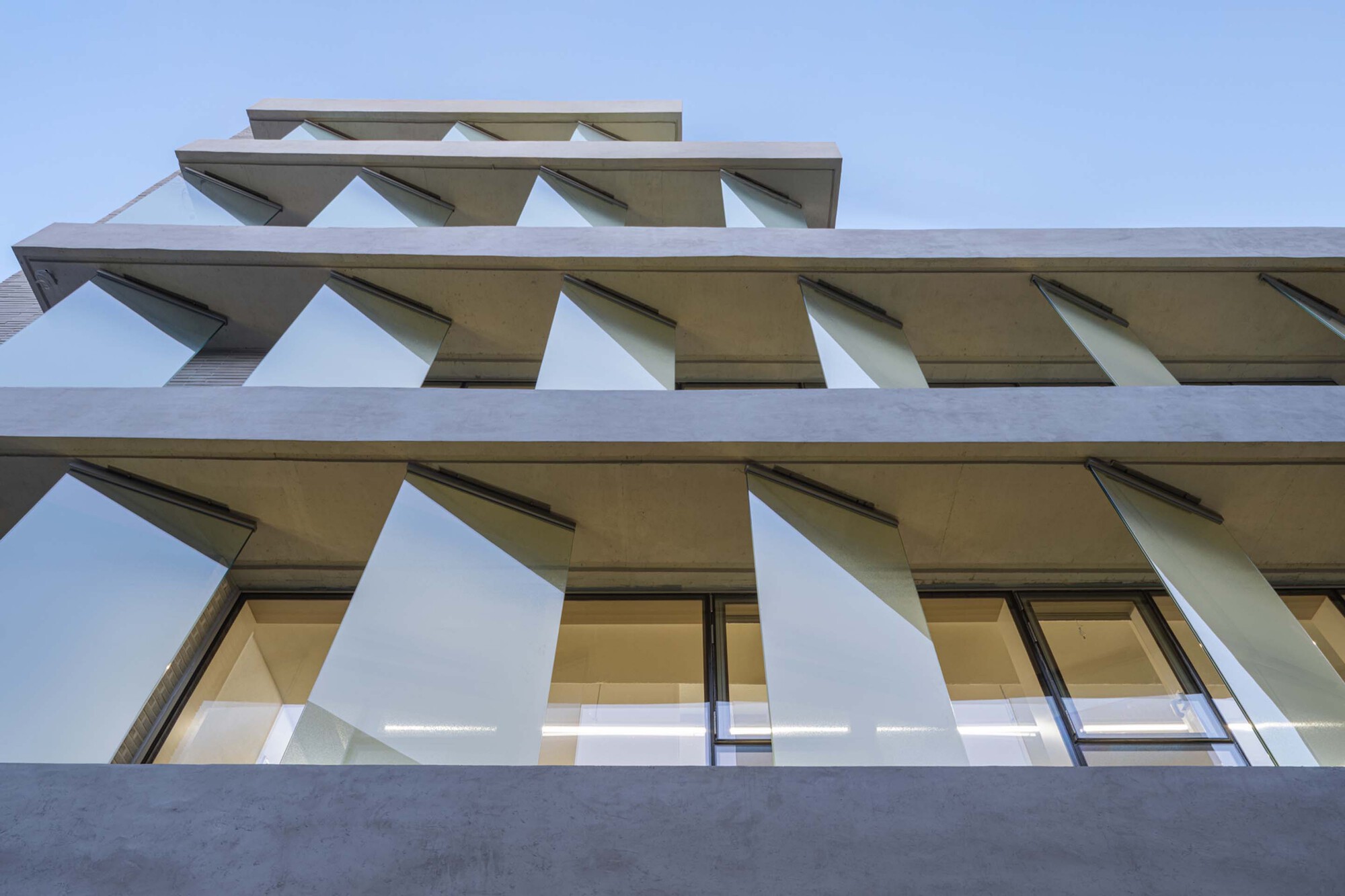 Upward view of stacked concrete balconies with angled white sunshades under a clear sky