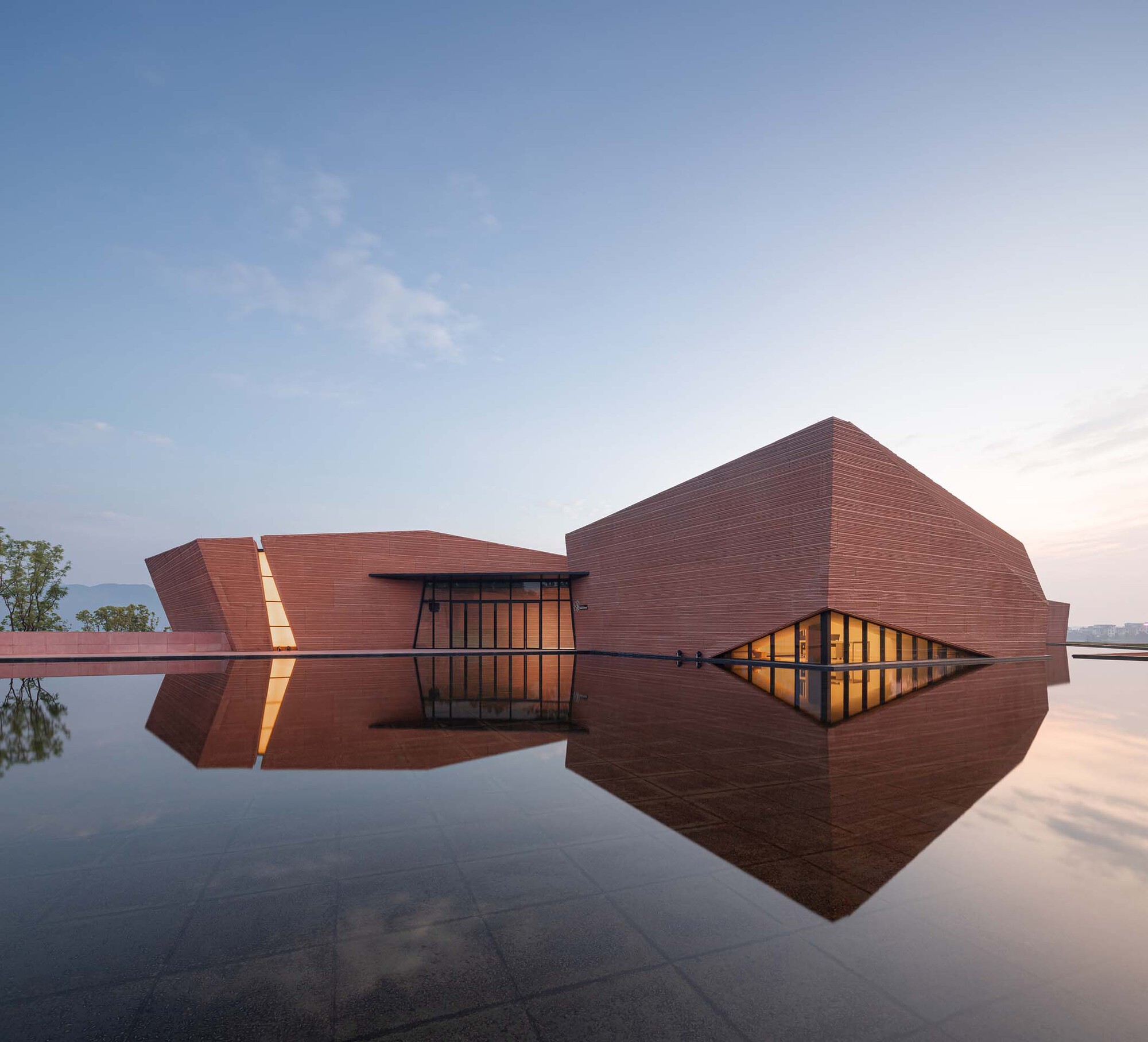 Horizontal red brick volumes reflected in a still water pool at dusk