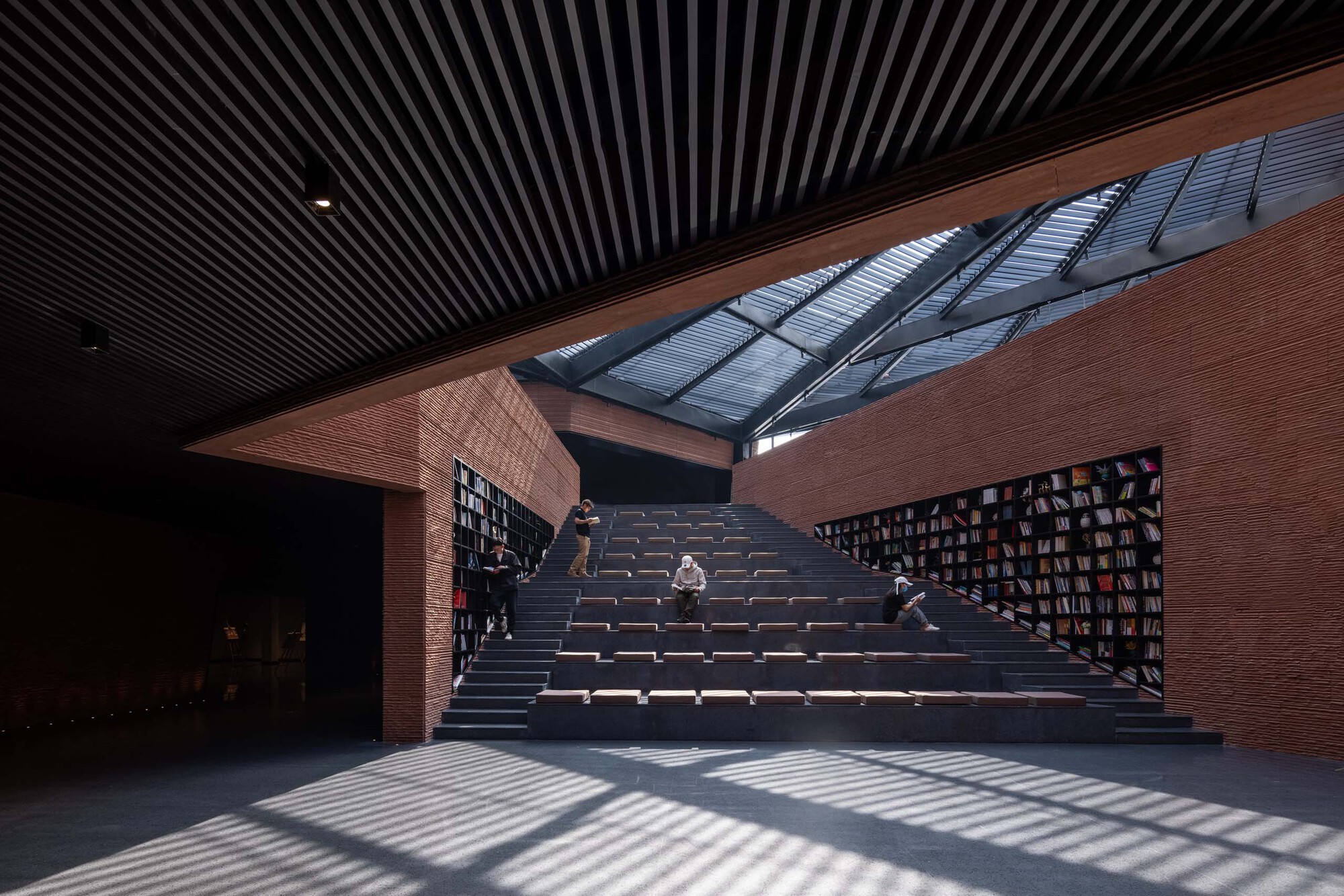 Interior auditorium stairs with slatted black ceiling and visitors sitting on timber treads
