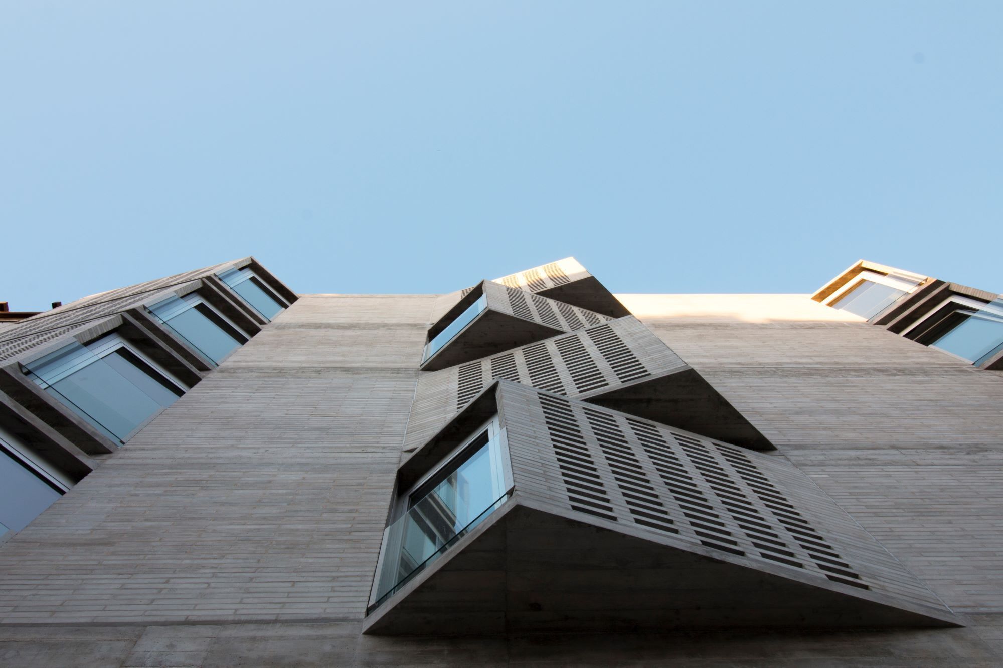 Worm's-eye view of angled bay windows and louvered sunscreens projecting from the concrete facade against clear blue sky
