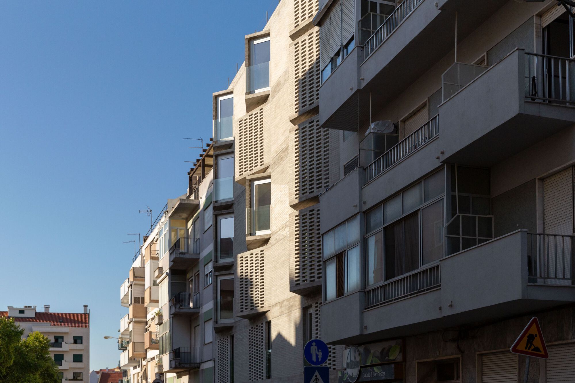 Street facade with cream-colored perforated brick towers and balconies under a clear blue sky