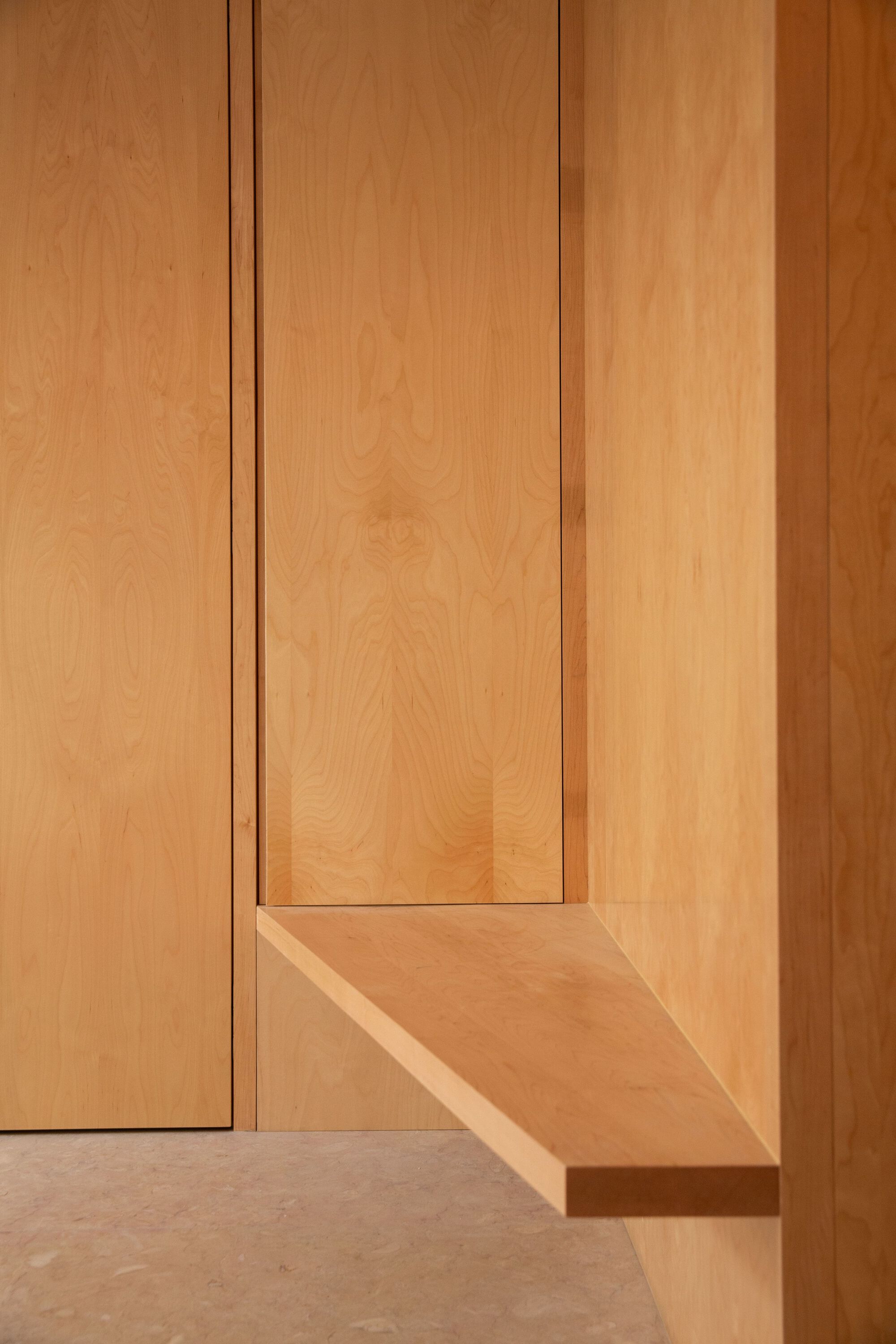 Detail of recessed timber panel corner meeting a stone floor in warm natural light