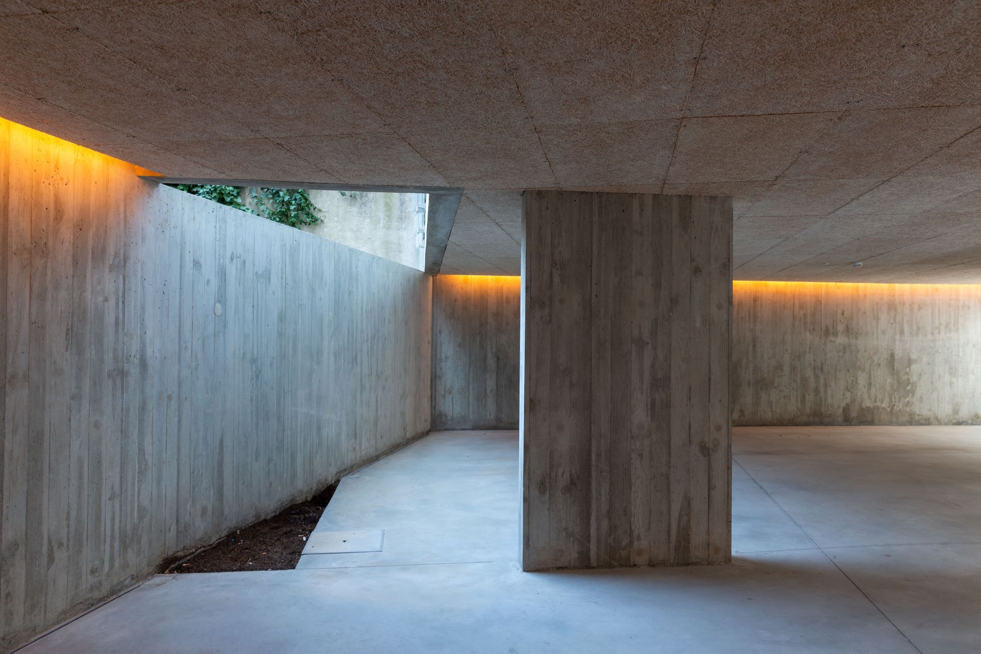 Board-formed concrete carport with indirect lighting strips illuminating walls and ceiling at dusk