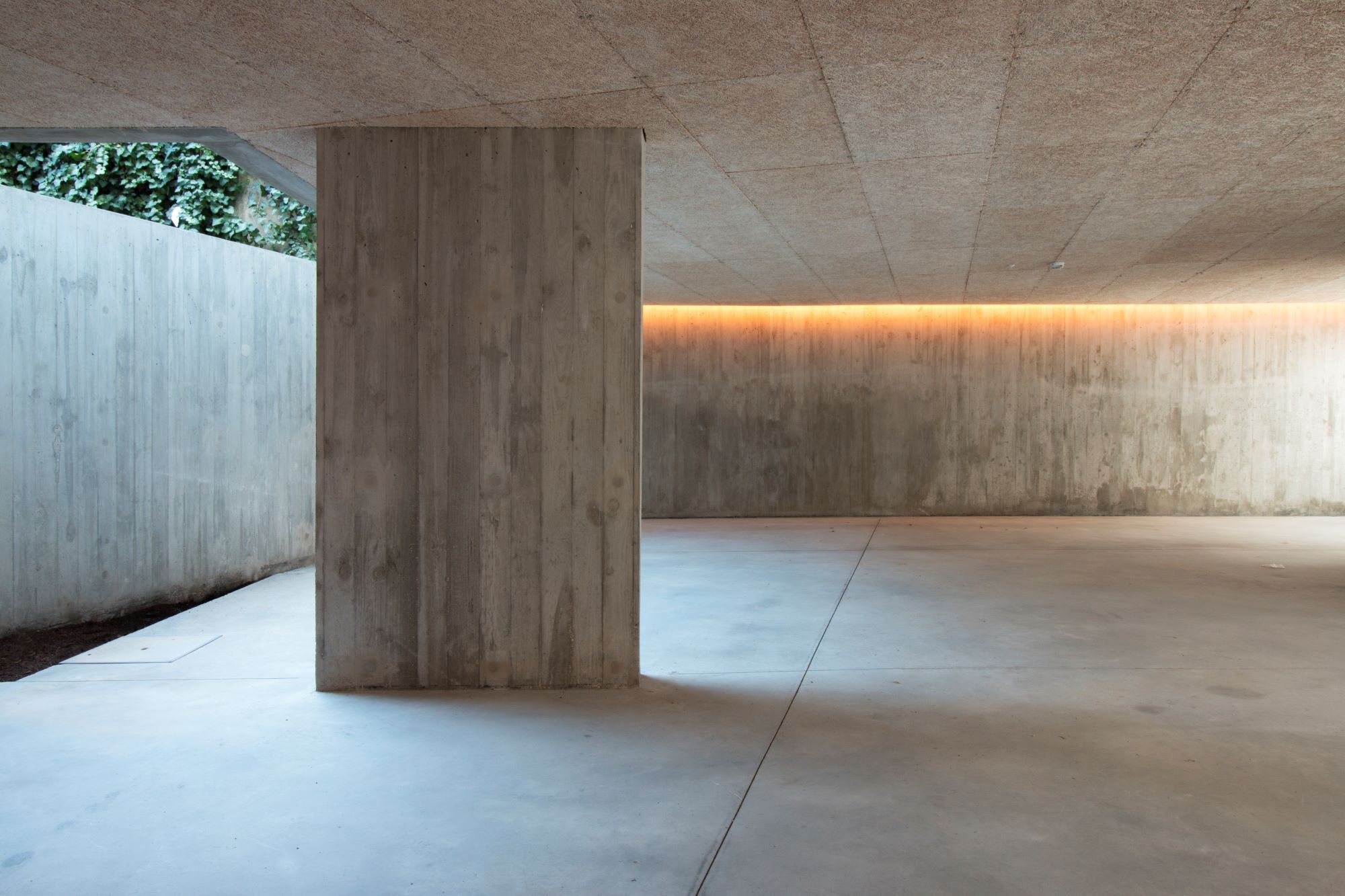 Covered concrete pavilion with timber-clad column, board-formed walls and recessed indirect lighting at dusk