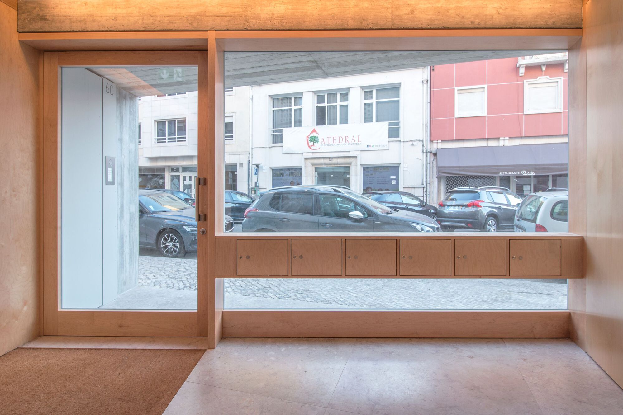 Interior timber-framed storefront with built-in bench looking out to a cobblestone street with parked cars