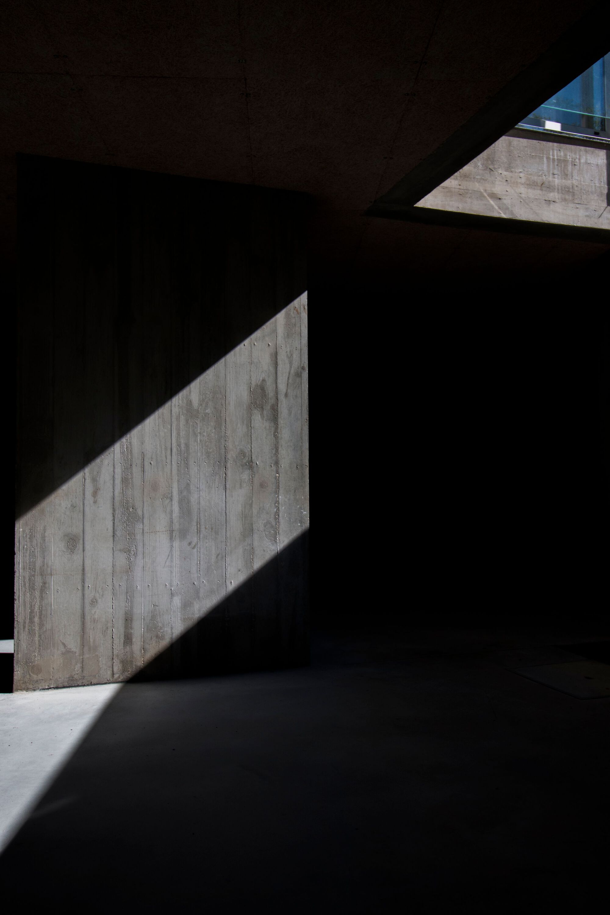 Diagonal light cutting across a darkened interior space with board-formed concrete walls