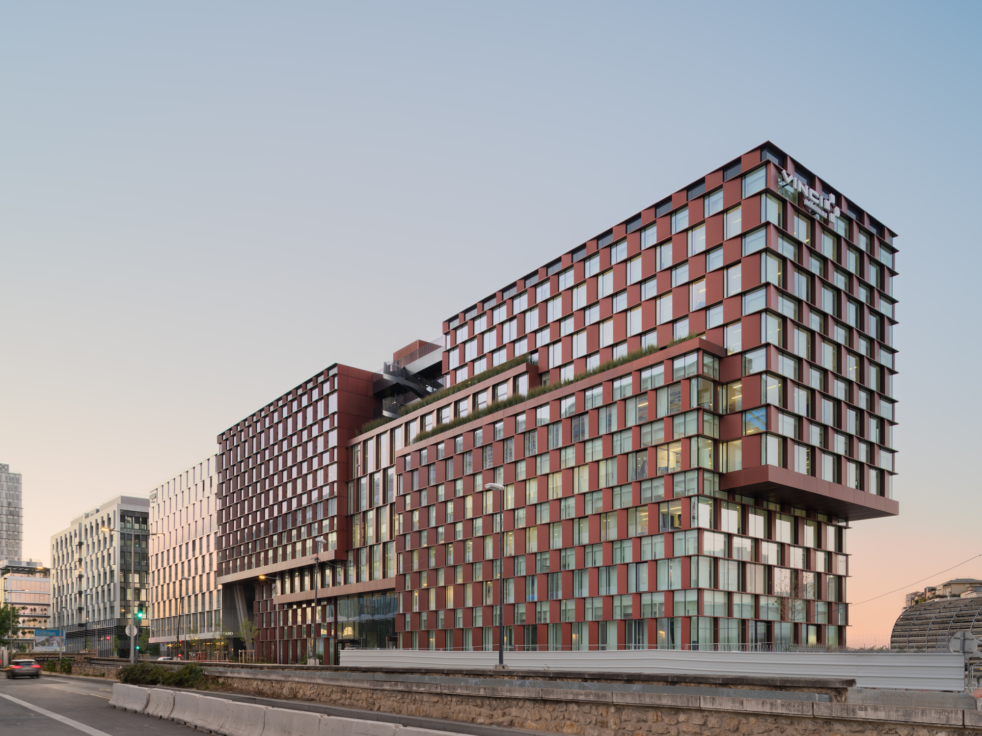 Street view of the chequered red and white panel facades arranged in stacked volumes at dusk