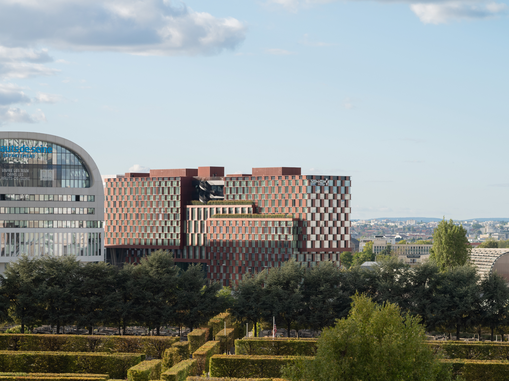 Distant view of the multi-volume facade rising above a landscaped foreground with mature trees